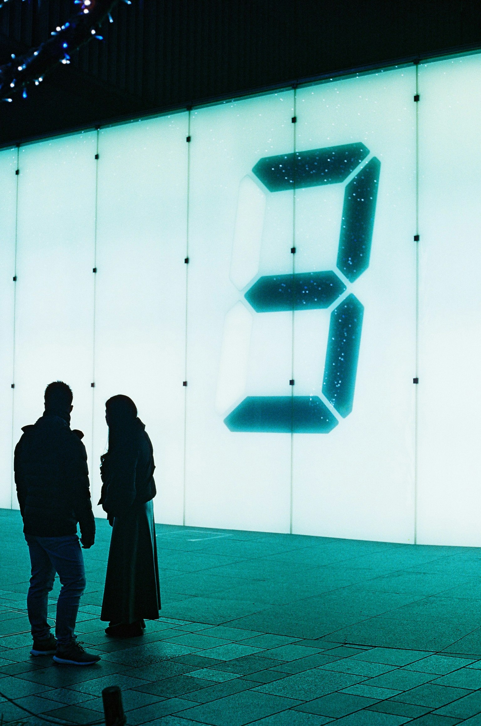 Silhouette de deux personnes devant un numéro 3 lumineux