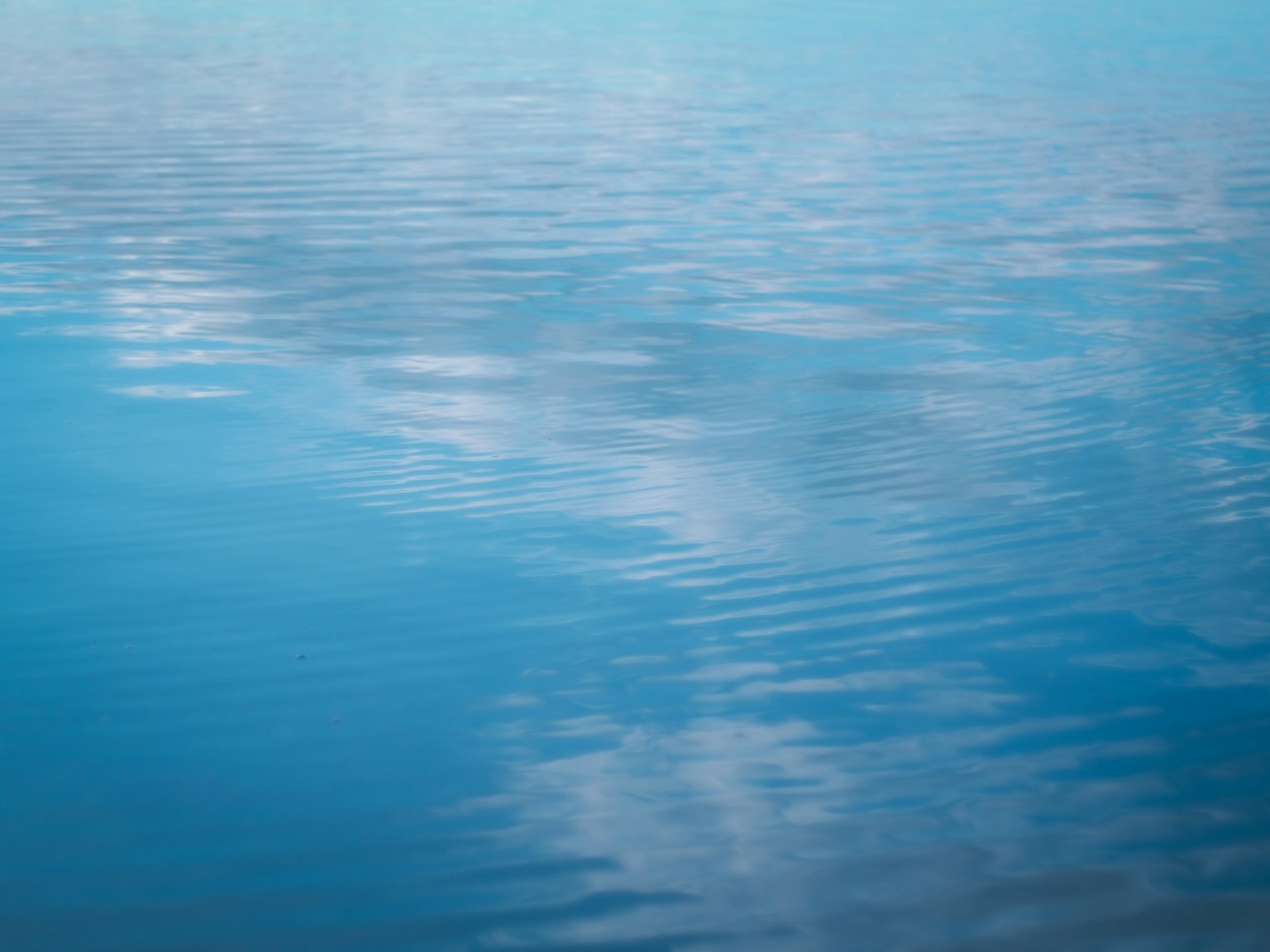 Superficie d'acqua blu calma che riflette le nuvole