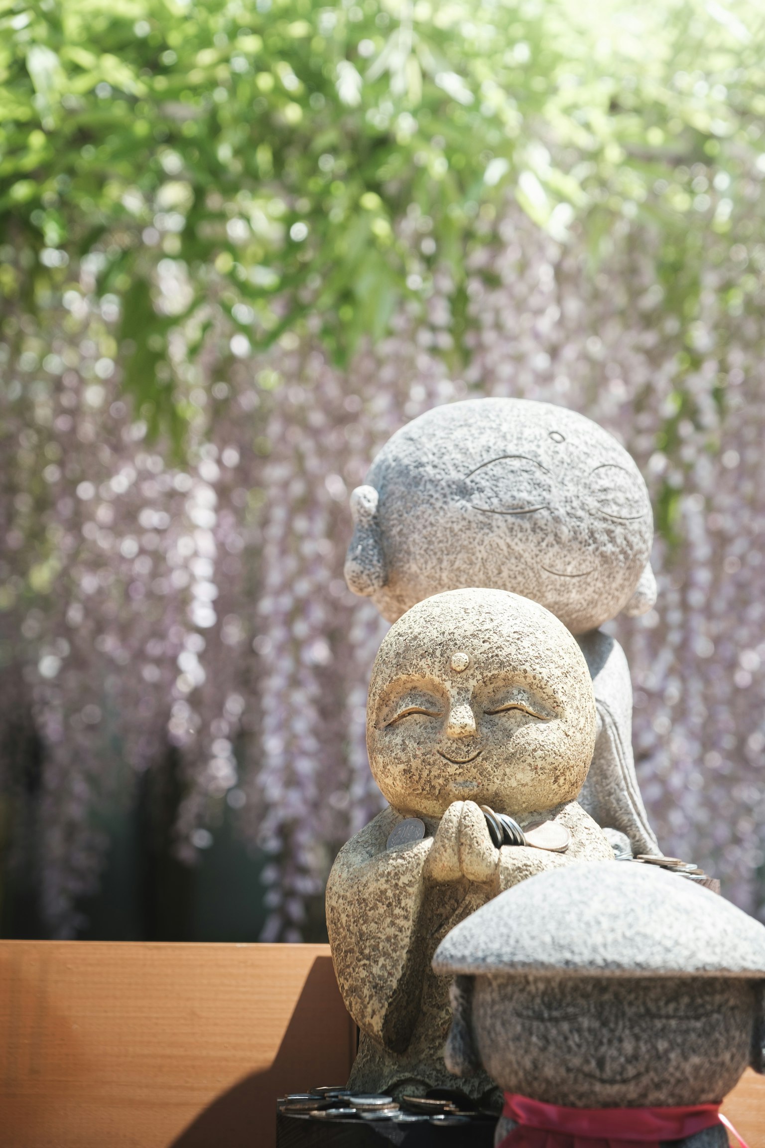 Statue en pierre d'un enfant et d'un adulte en prière avec des fleurs de glycine en arrière-plan