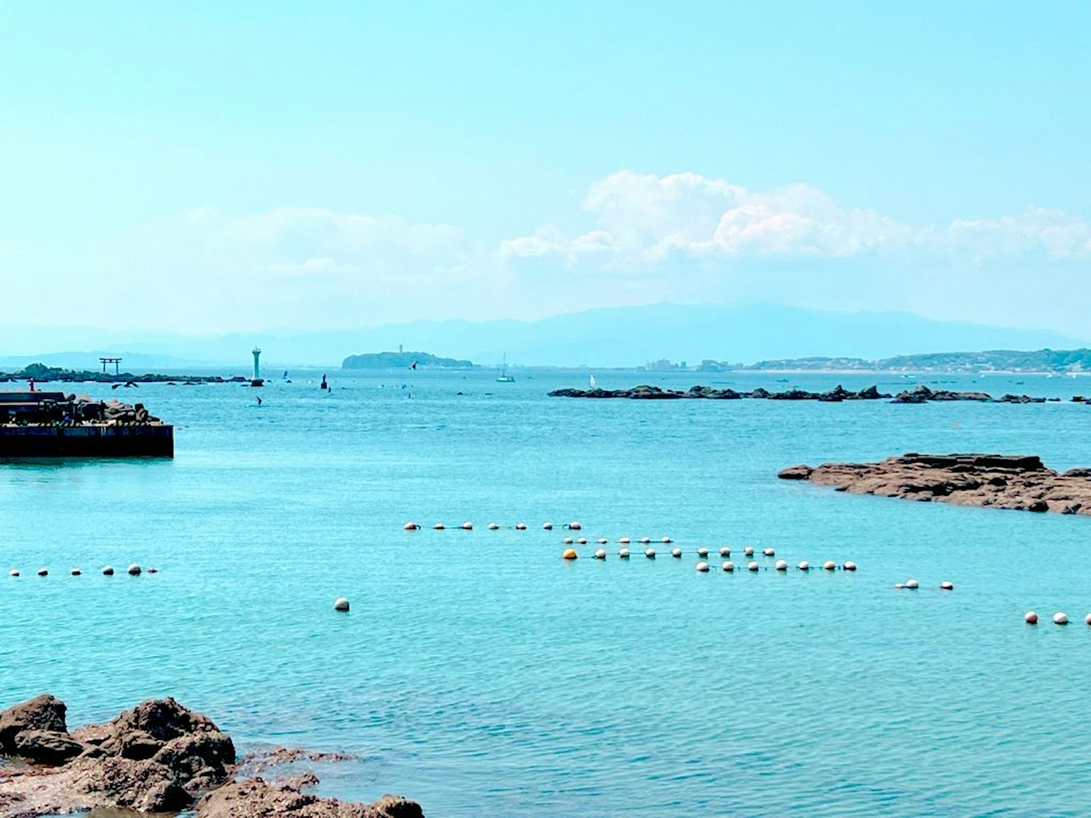Malersiche Aussicht auf ein blaues Meer mit felsiger Küste und schwimmenden Bojen im klaren Wasser