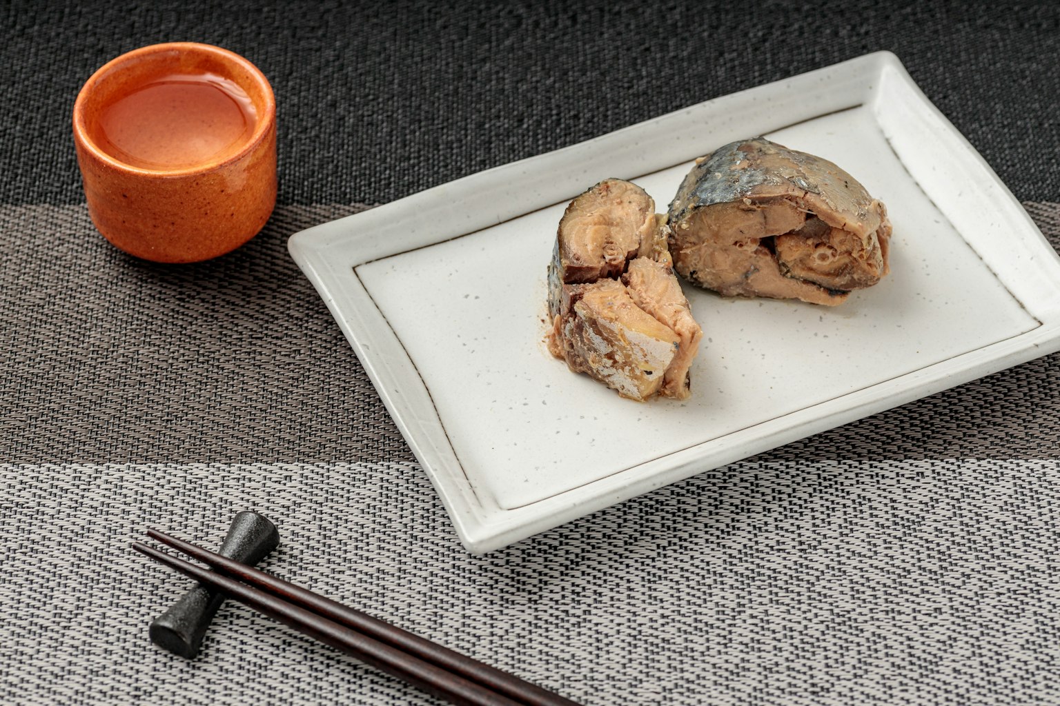Fish dish served on a white plate with a small orange cup of beverage