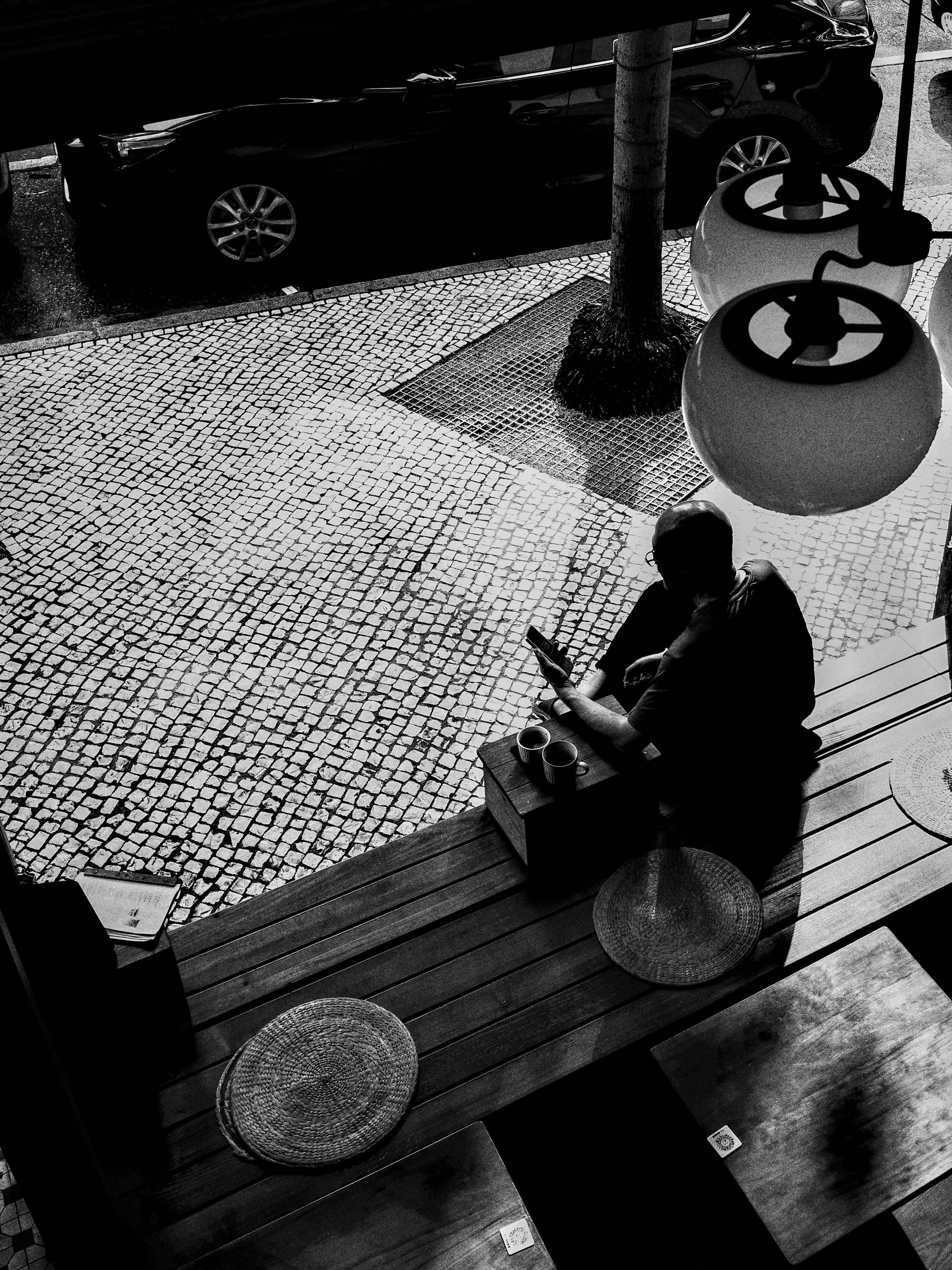 monochrome scene of a person relaxing on a wooden bench by a cobblestone lane