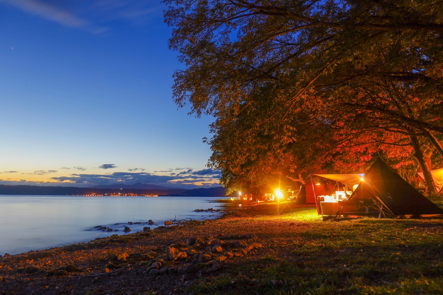 Tranquil lakeside campsite at dusk bright lamps and trees illuminated