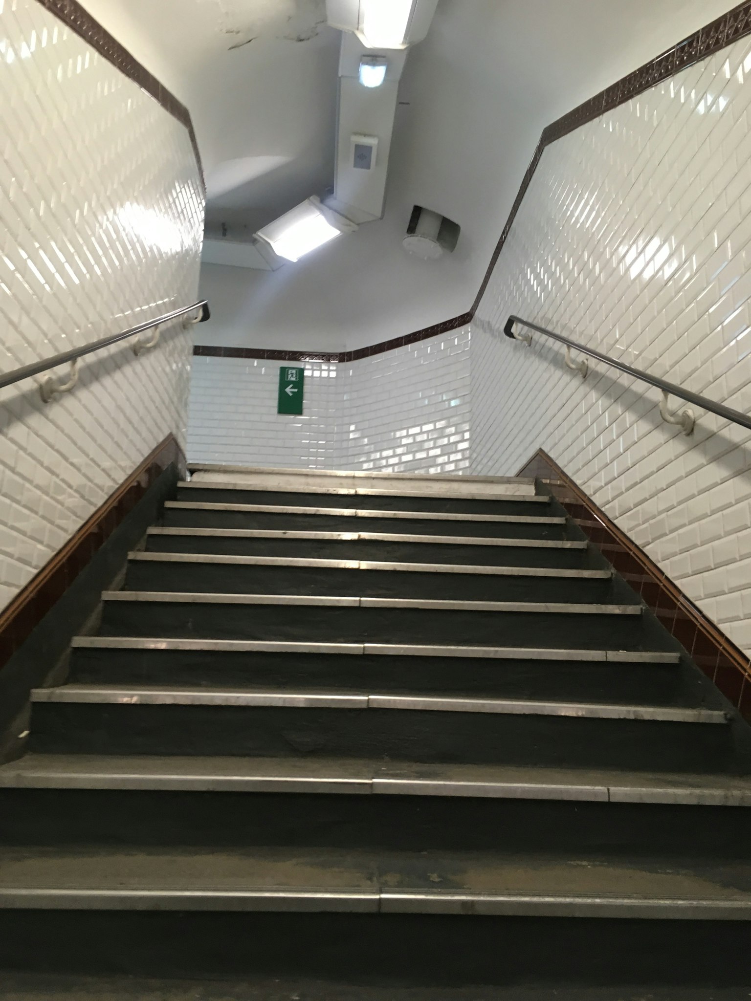 Vue des escaliers depuis le bas avec des murs carrelés blancs et des rampes