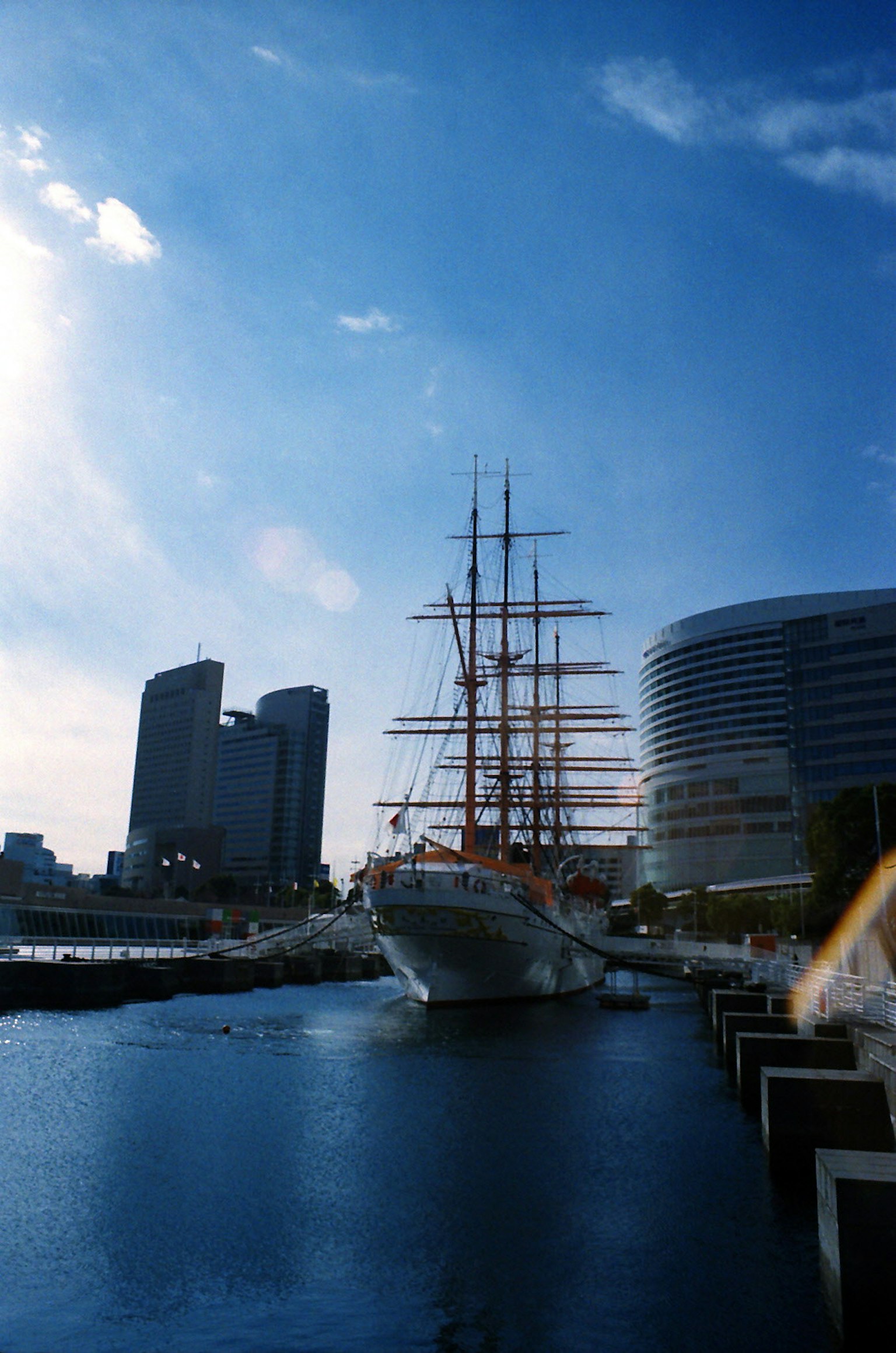 Barco de vela atracado bajo un cielo azul con edificios modernos