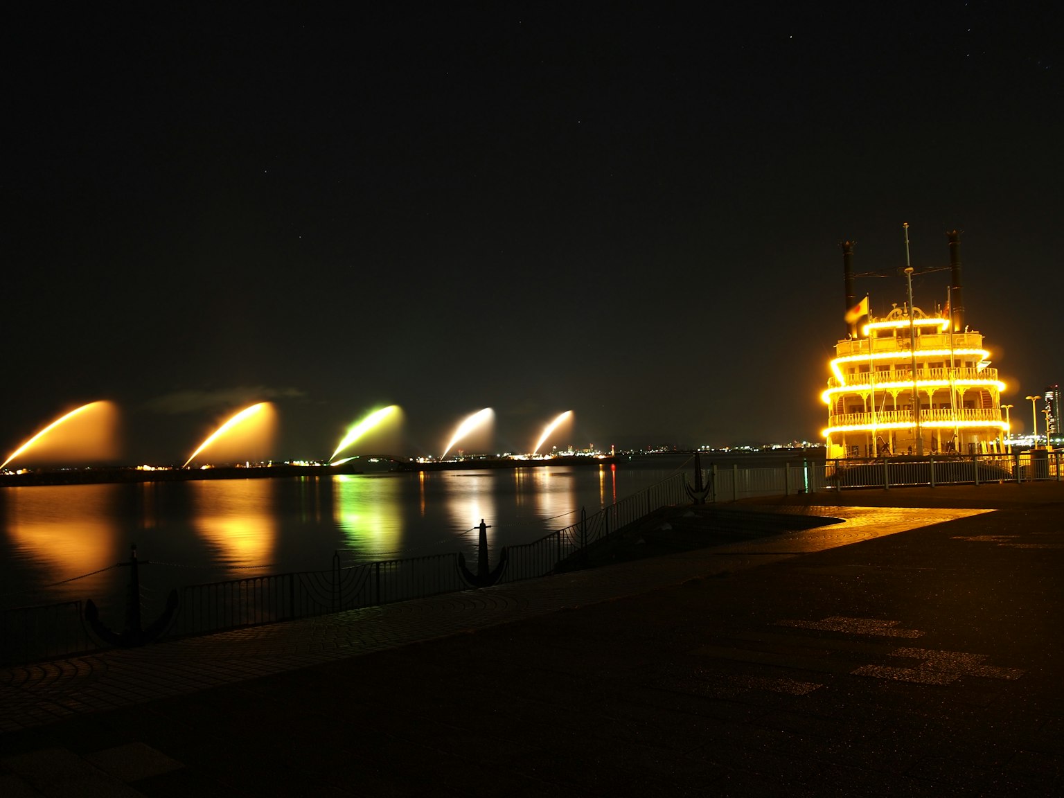 Bateau illuminé sur la rivière la nuit avec des lumières de fontaine colorées