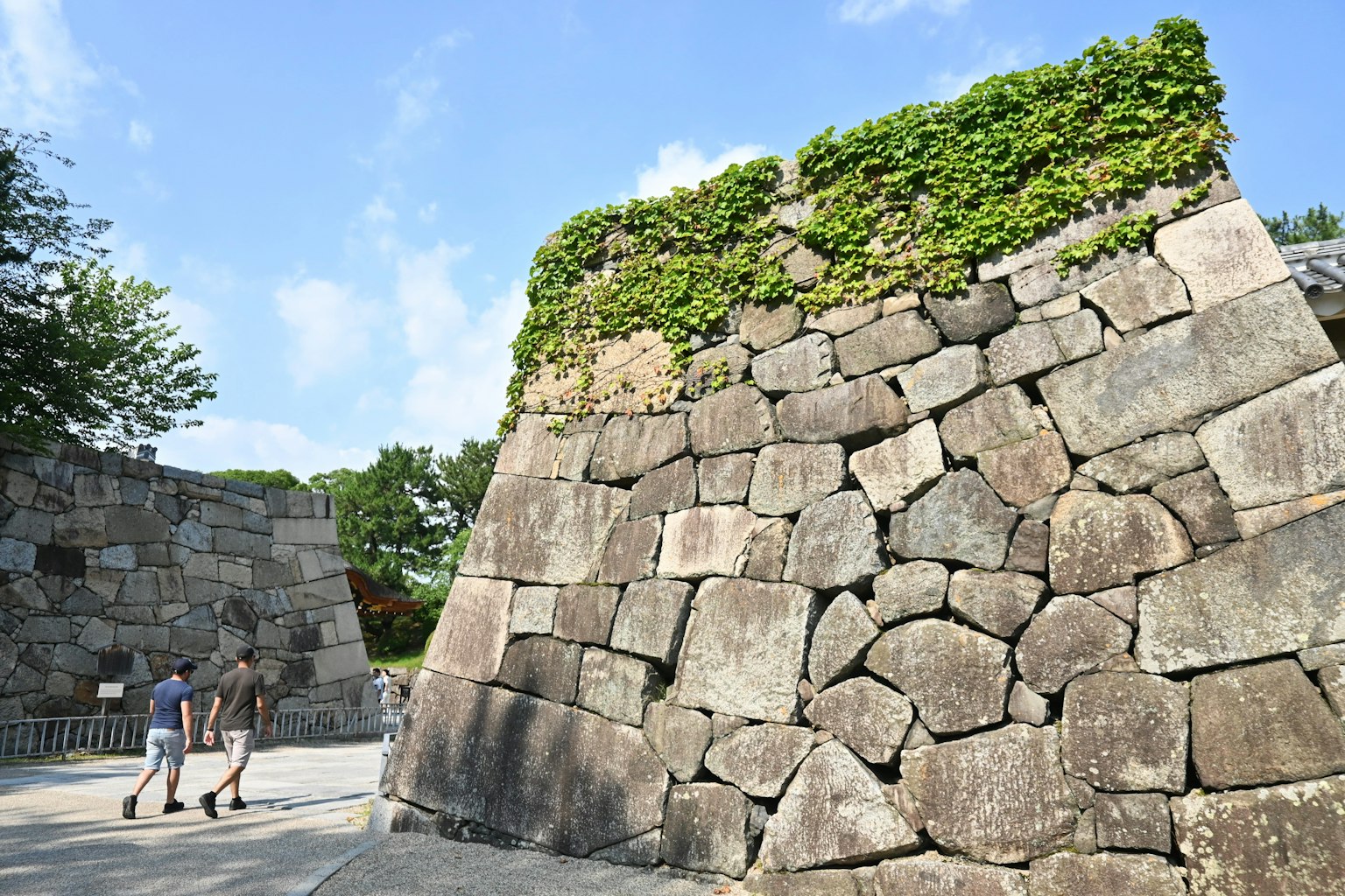 Two tourists walking near a stone wall covered with greenery at a castle