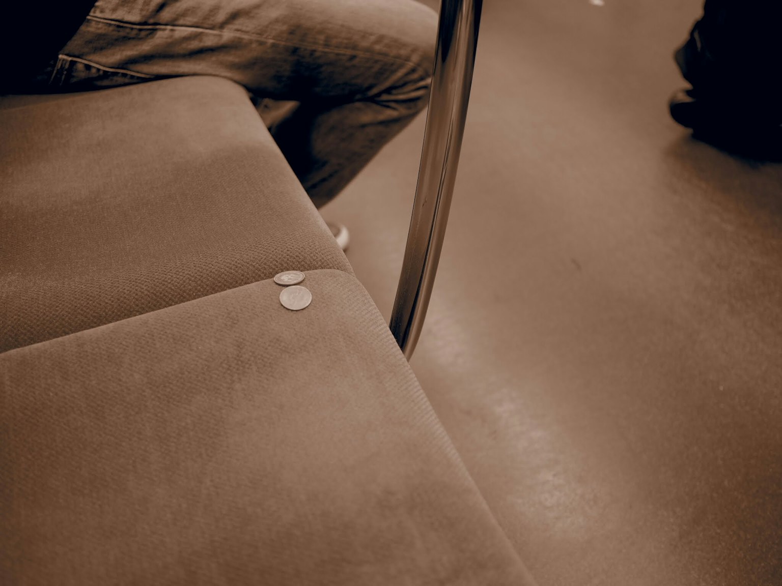 Coins placed on a subway seat with a passenger's leg visible