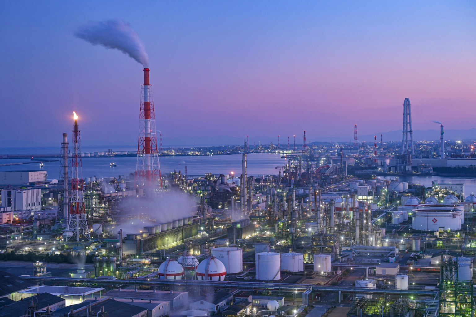 Area industriale al crepuscolo con fumi che escono dai camini e fabbriche illuminate