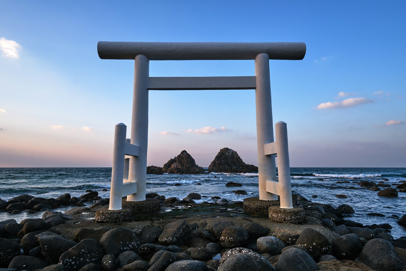 Weißes Torii mit Blick auf den Ozean bei Sonnenuntergang schafft eine friedliche Atmosphäre