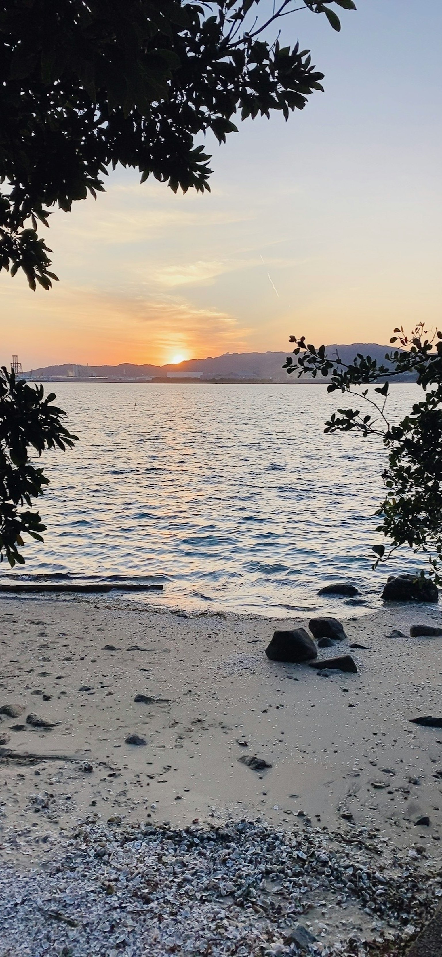 วิวชายหาดพร้อมพระอาทิตย์ตกเหนือทะเลและมีหินมองเห็นได้