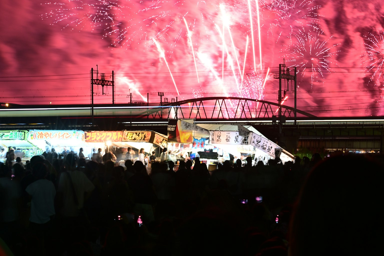 Feuerwerke erhellen den Nachthimmel über einer Brücke und einer Menge