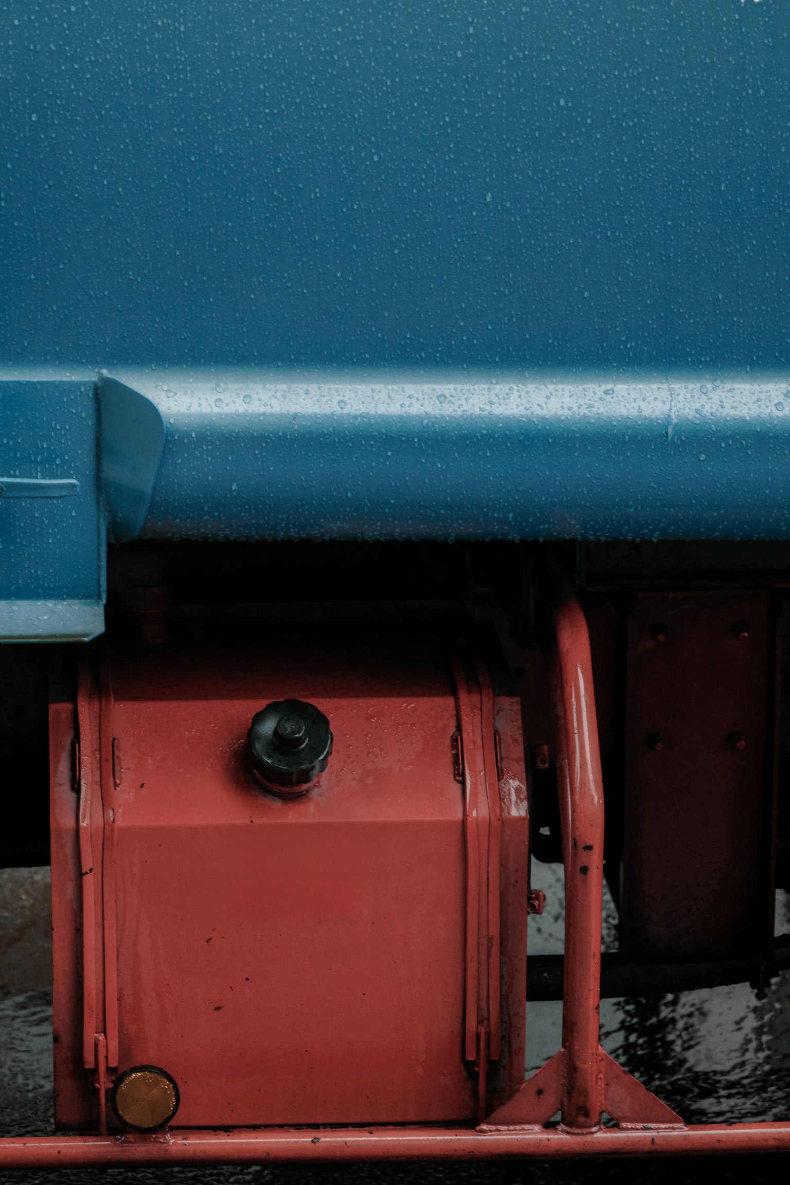 Réservoir rouge sous un véhicule bleu avec des gouttes de pluie