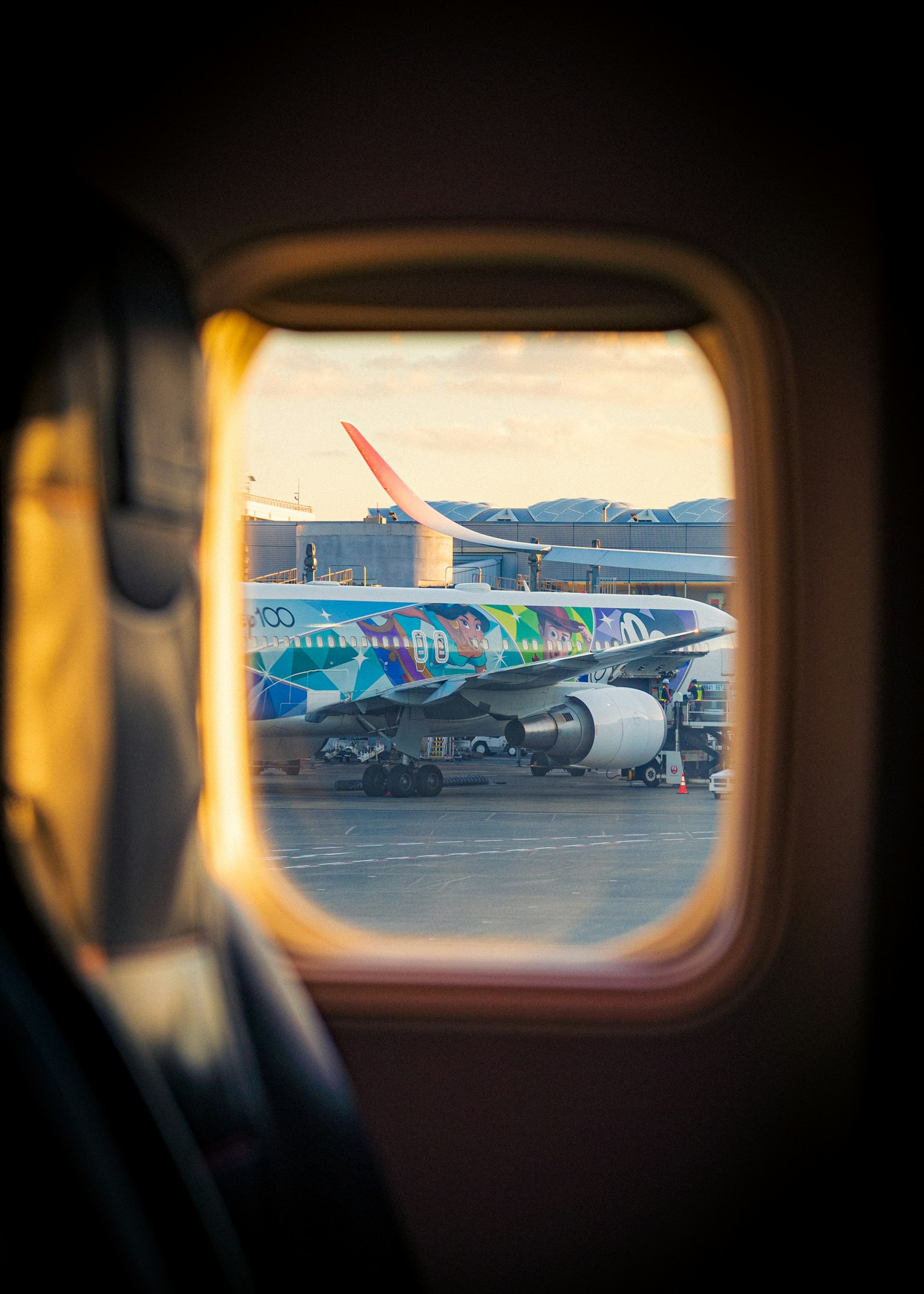 Blick auf ein buntes Flugzeug durch ein Fenster mit Flughafenlandschaft