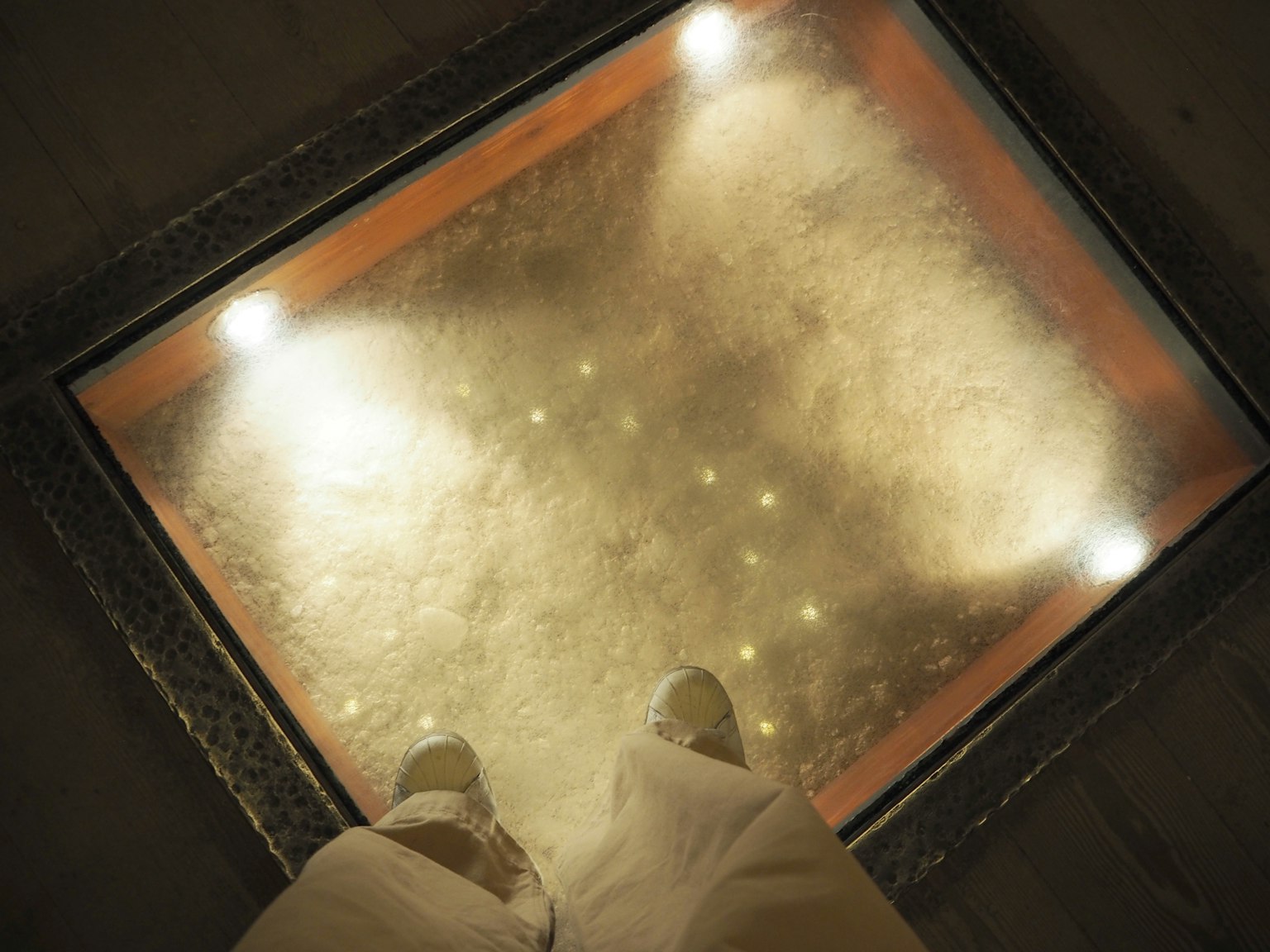 View from above of a person's feet standing on a transparent floor with glowing lights and patterns