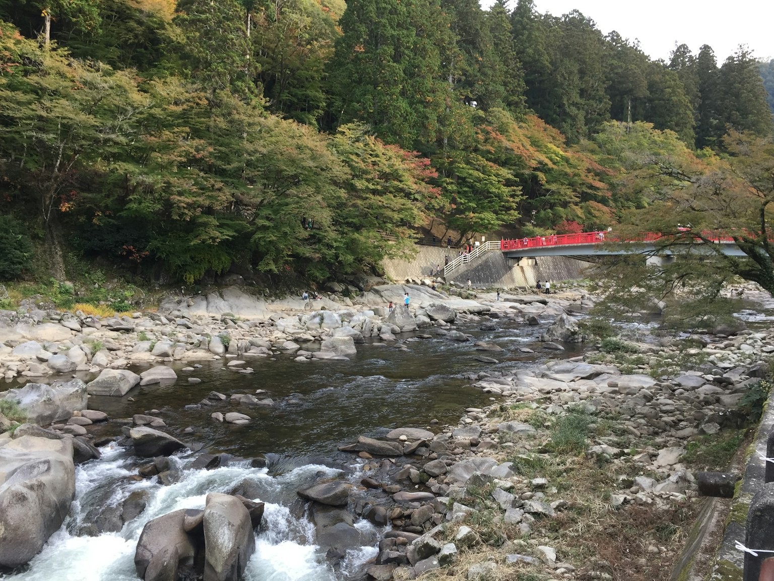 Malersicher Fluss mit fließendem Wasser und Steinen roter Brücke und grünen Bäumen