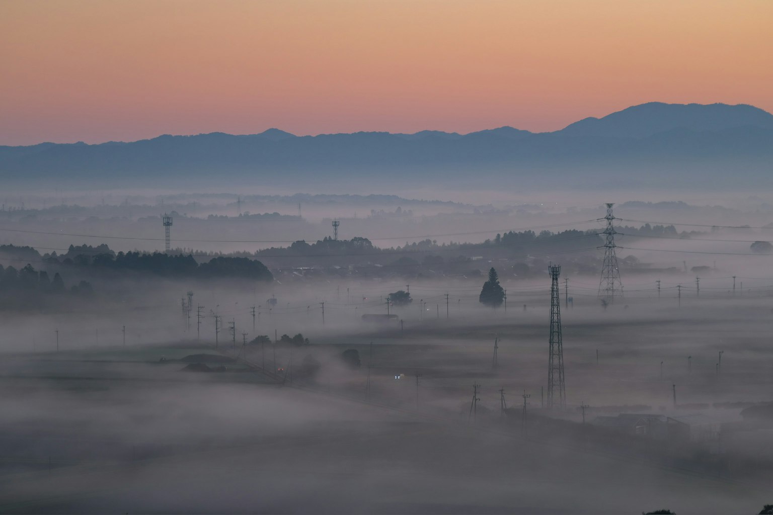 Paisaje cubierto de niebla con siluetas de montañas y líneas eléctricas al amanecer