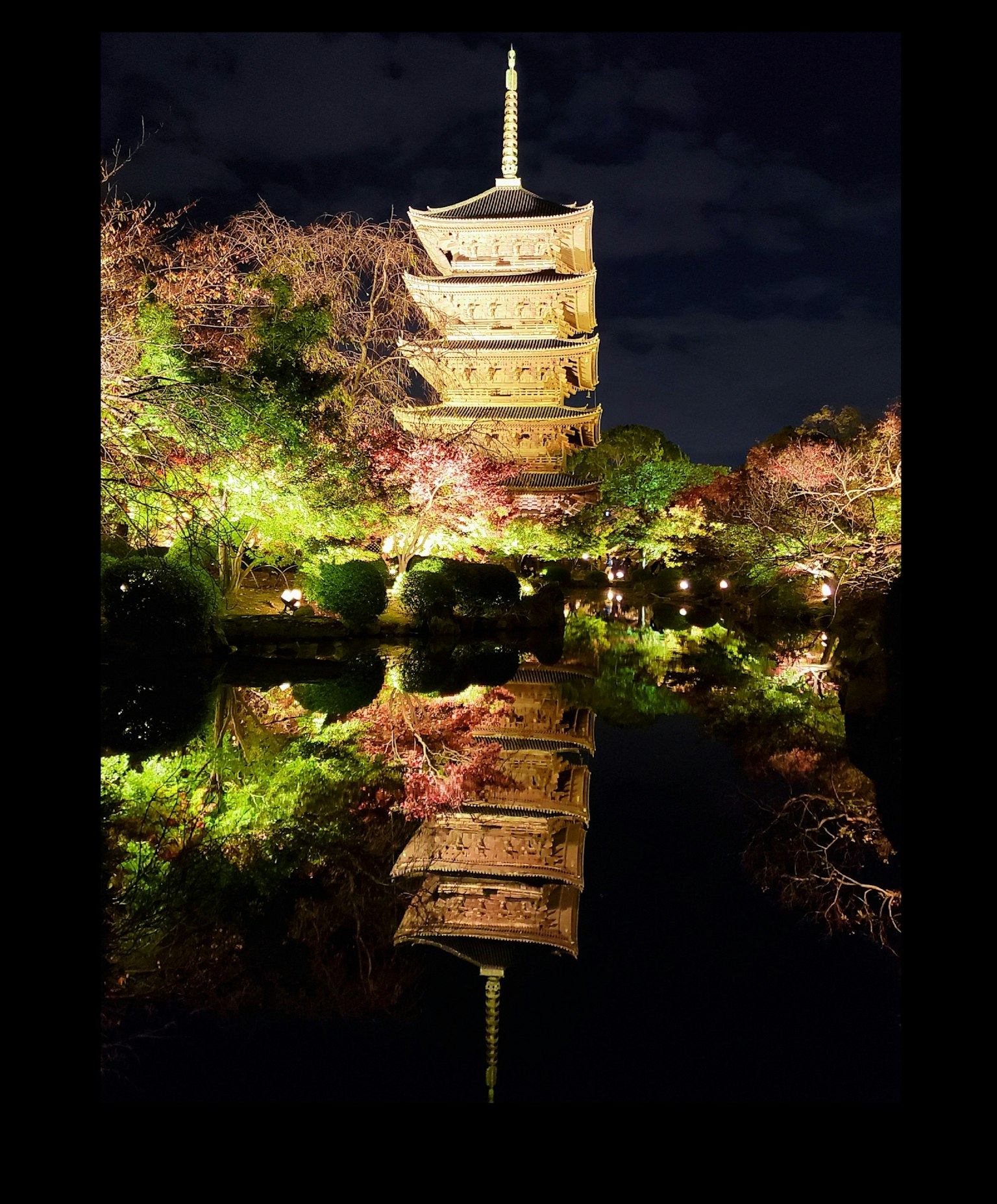 夜晚美丽照亮的五重塔在宁静的池塘中反射，周围环绕着樱花