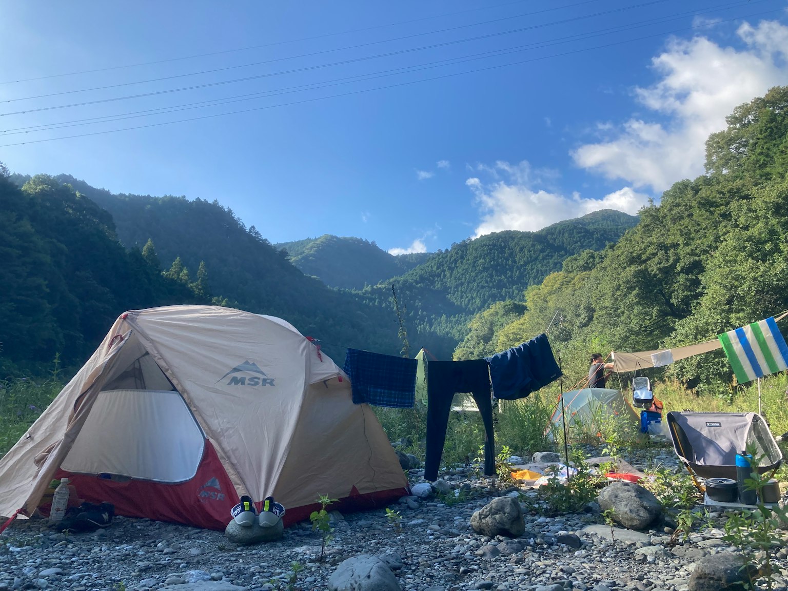 Ein Campingplatz umgeben von Bergen mit einem Zelt und aufgehängter Wäsche