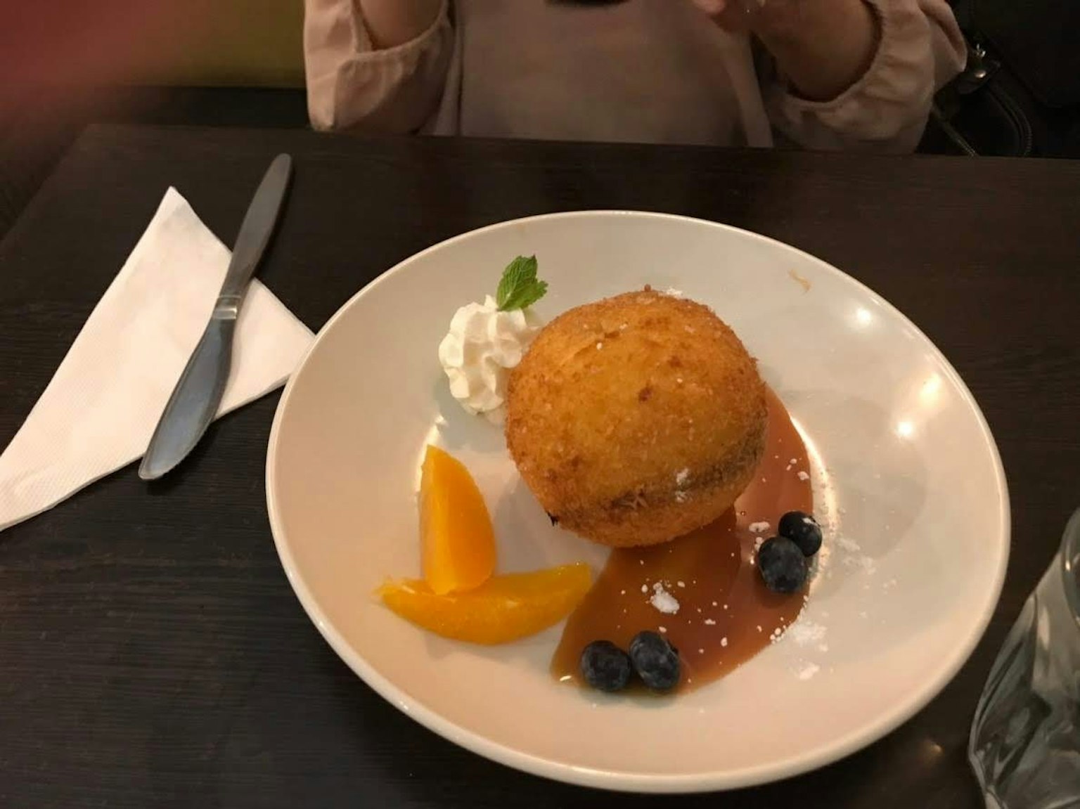 Palla di dessert fritta guarnita con panna e servita con fette di frutta in un piatto bianco