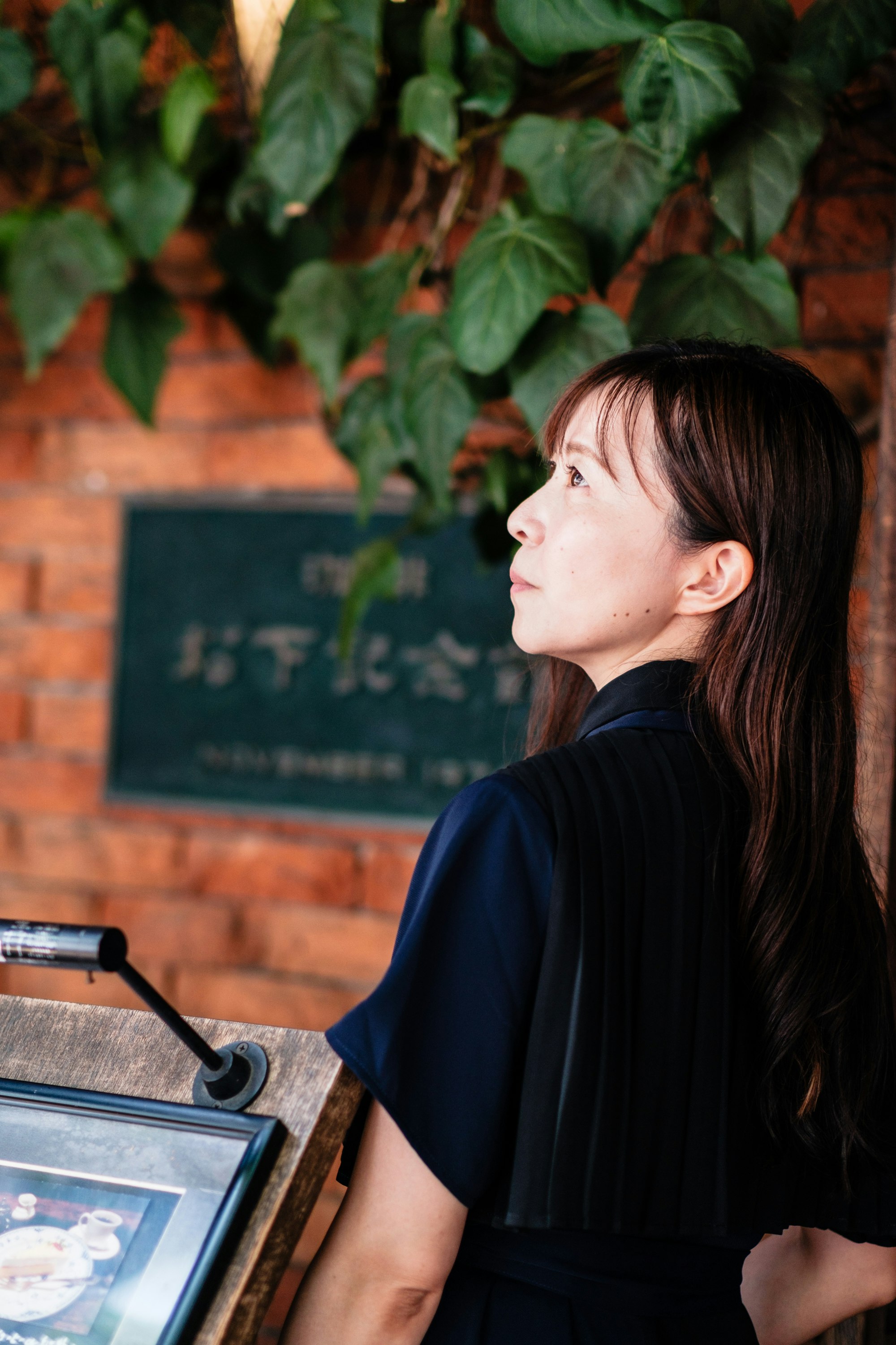 レンガ壁の前で黒い服の人物が掲示板を見上げる