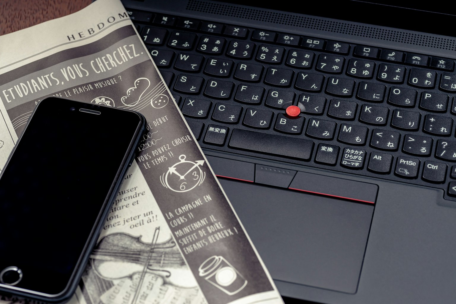 Tastiera del laptop con uno smartphone nero e un giornale