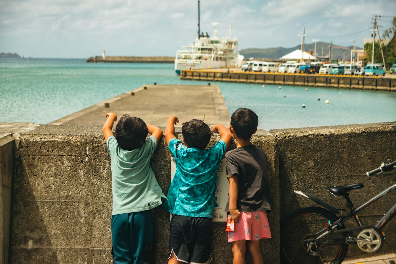 Anak-anak bersandar di dermaga melihat kapal di pelabuhan