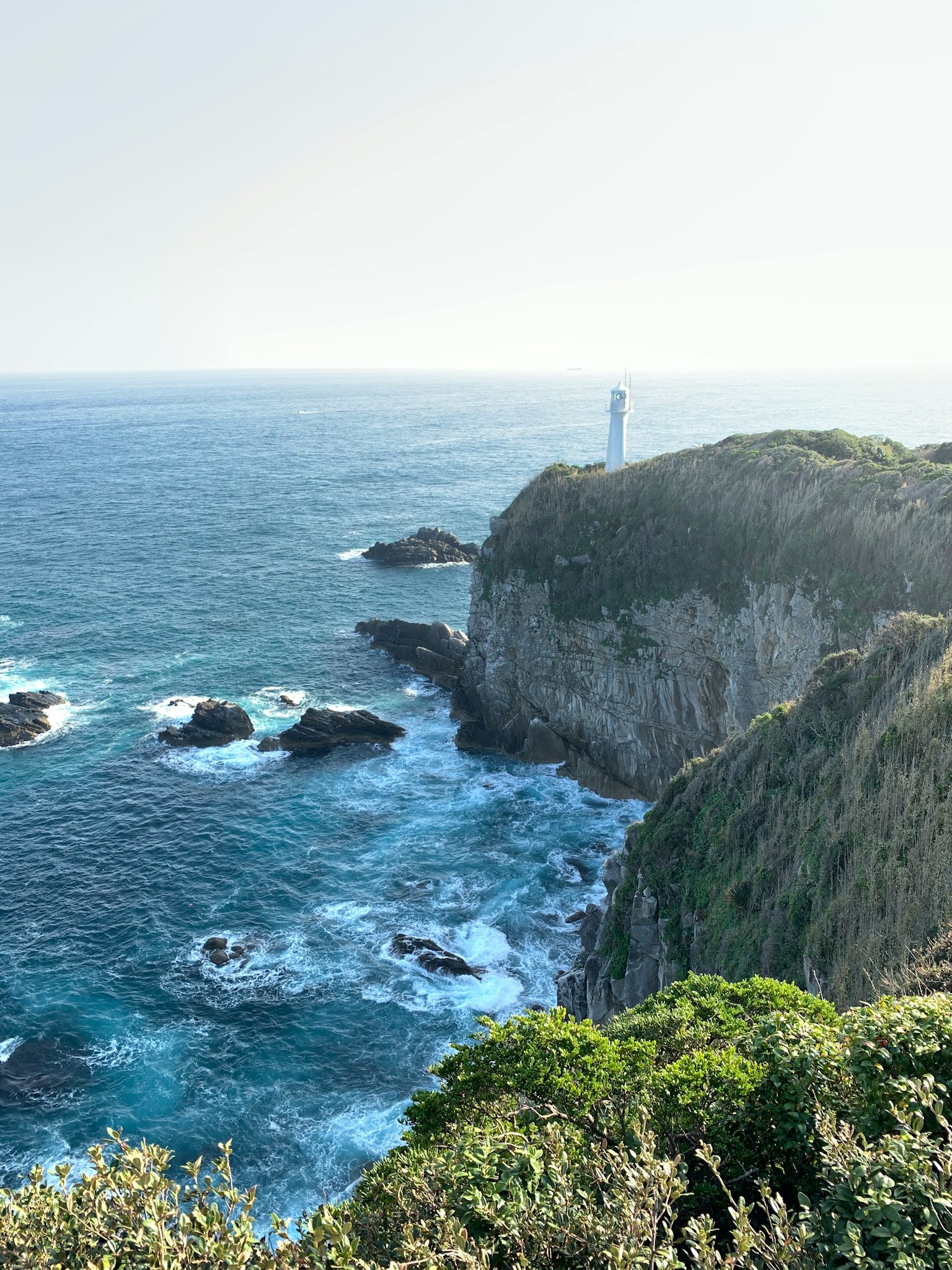 Coastal cliff with a lighthouse overlooking the blue sea and white waves