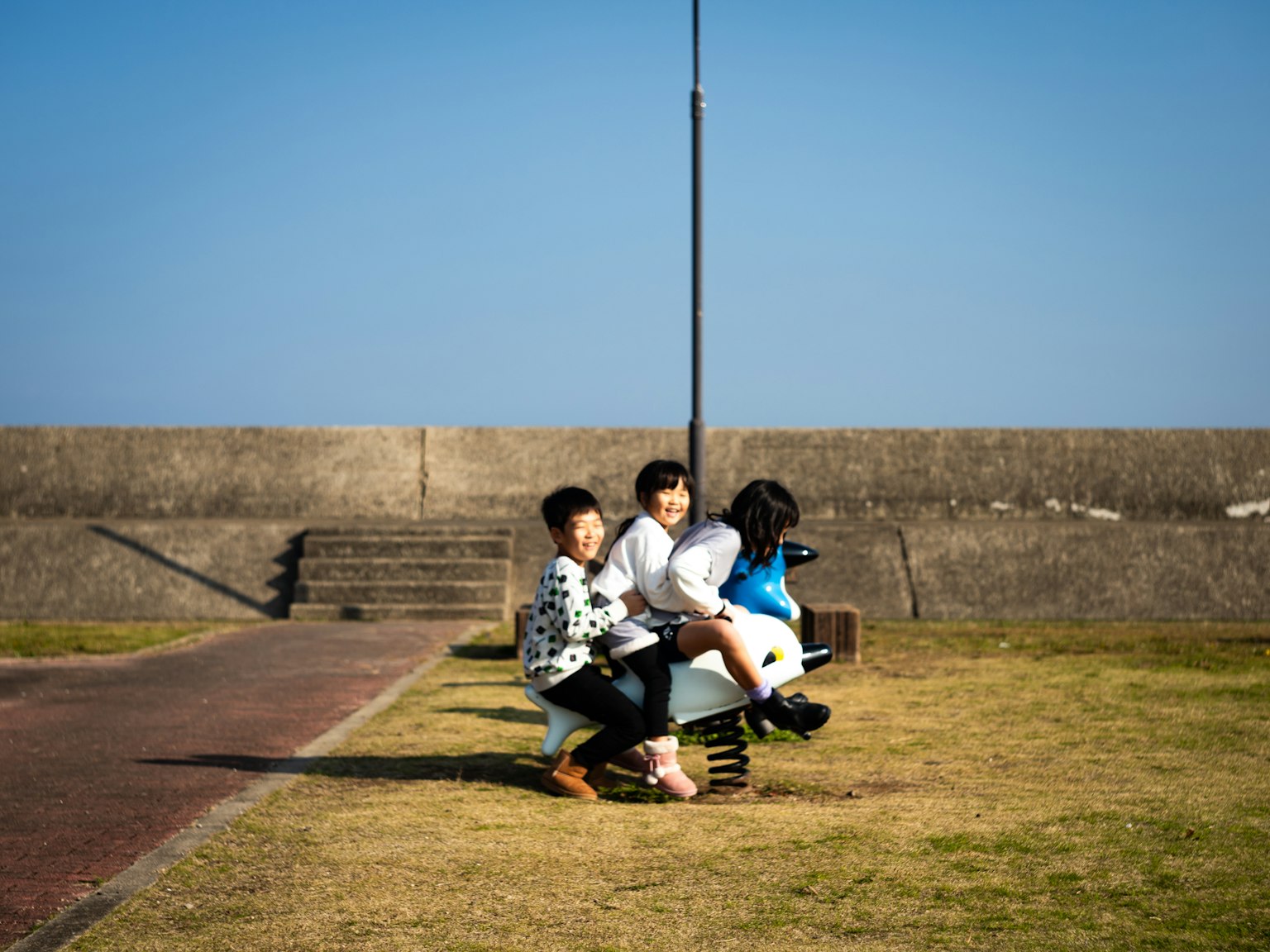 公園のベンチに座る子供たちの写真 青空と芝生のある風景