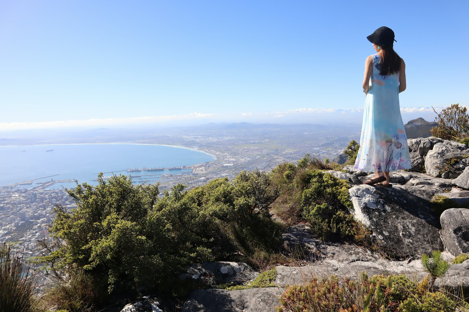 Una mujer de pie en la cima de una montaña mirando una hermosa vista del mar y la ciudad