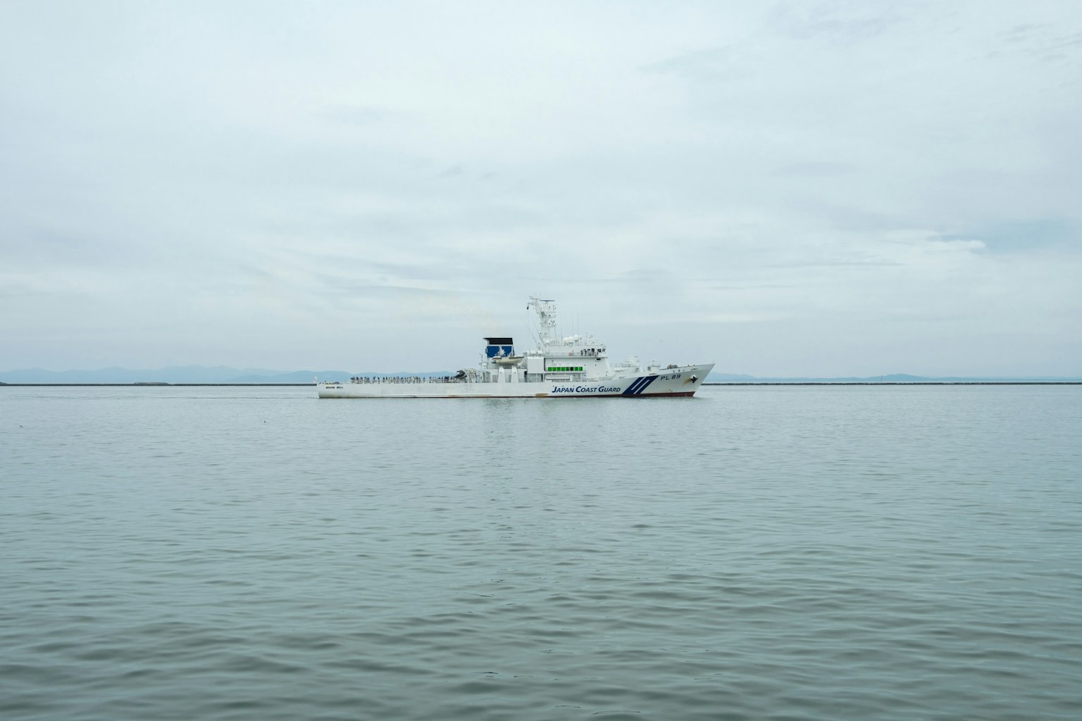 A white ship floating on calm waters under a gray sky