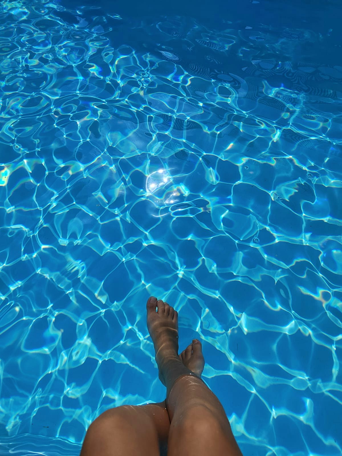 青いプールの水面に足を浸している女性の足