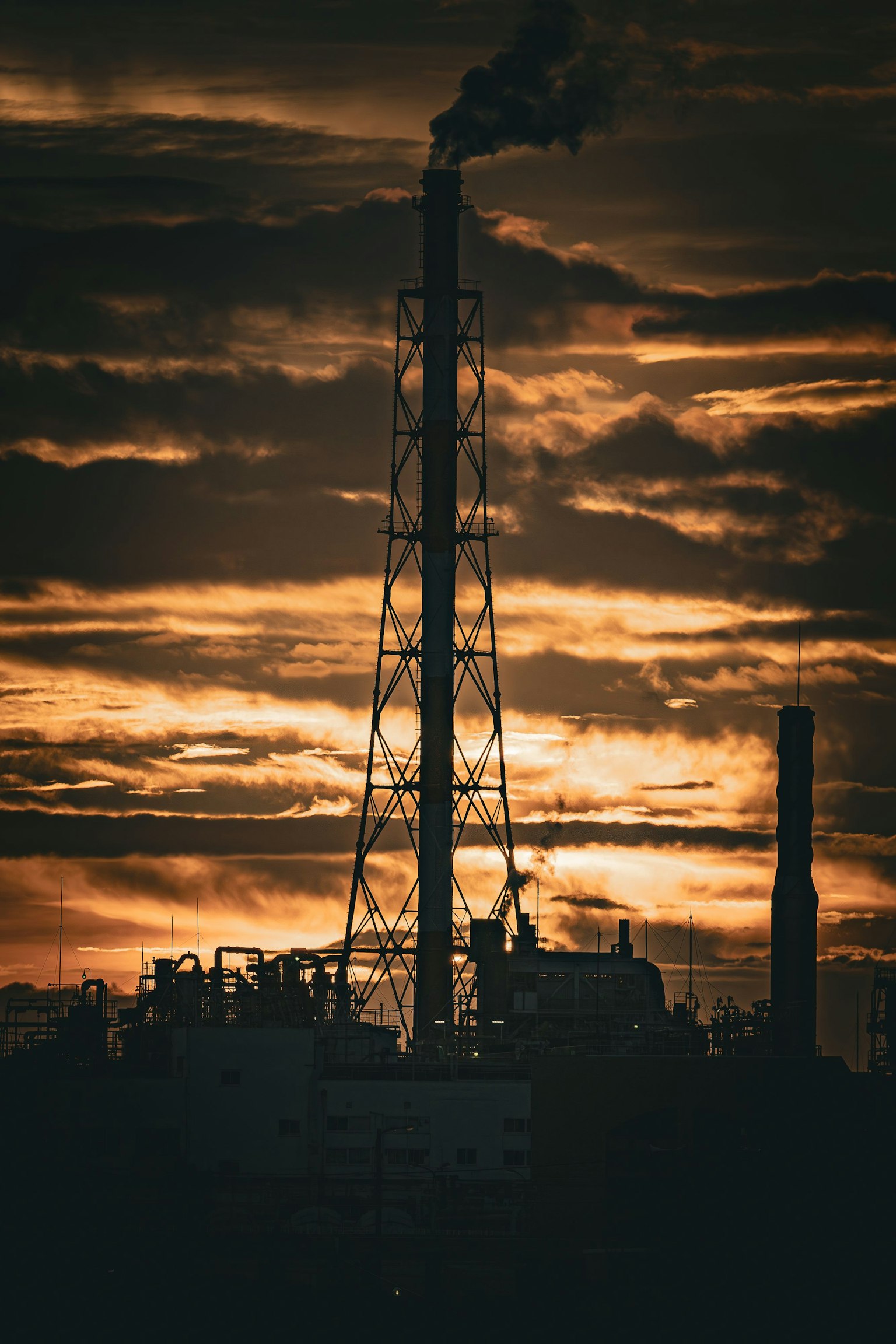 Silhouette eines Schornsteins und industrieller Strukturen vor einem Sonnenuntergangshimmel