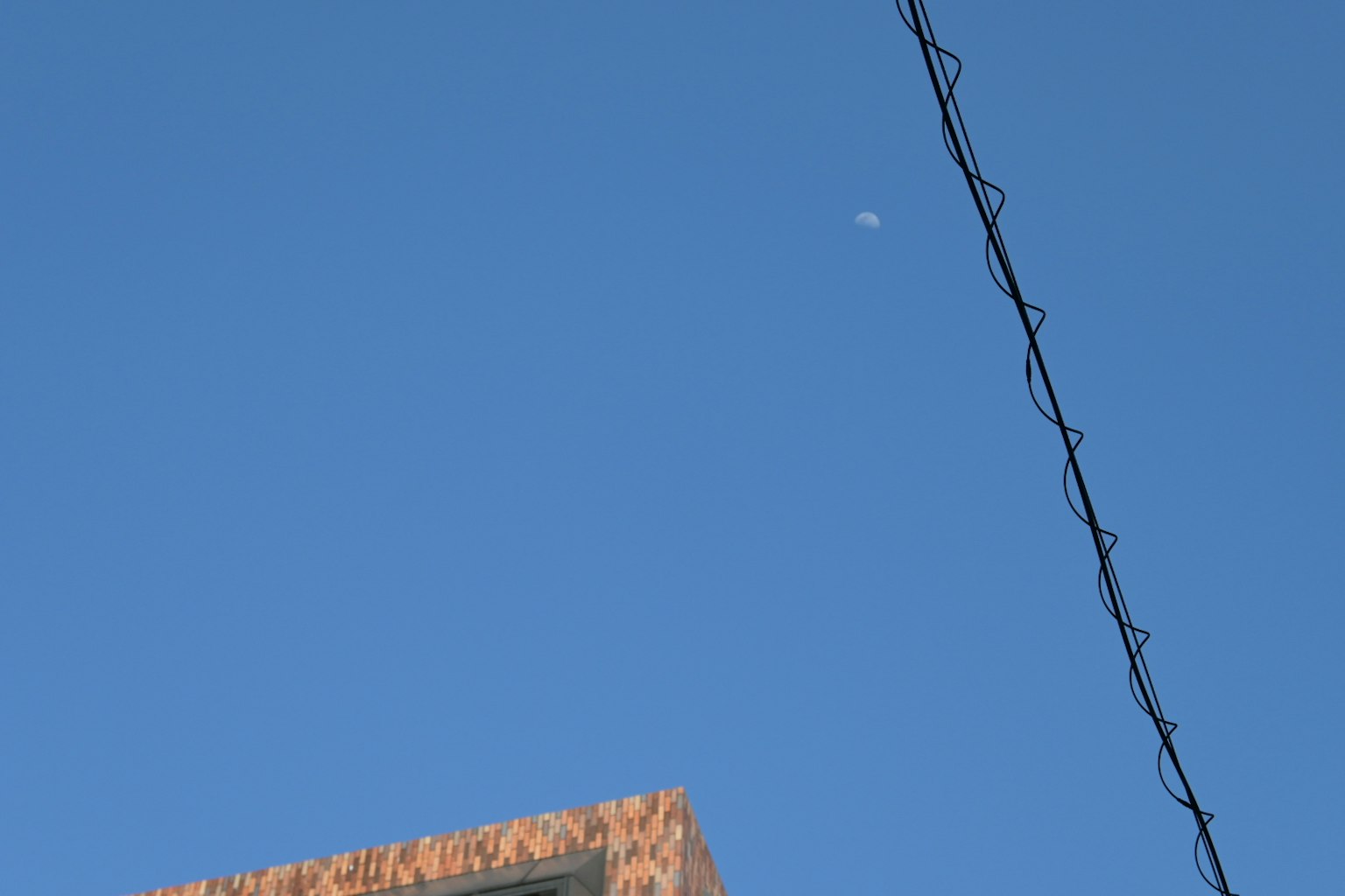 View of a clear blue sky with a small moon and part of a building