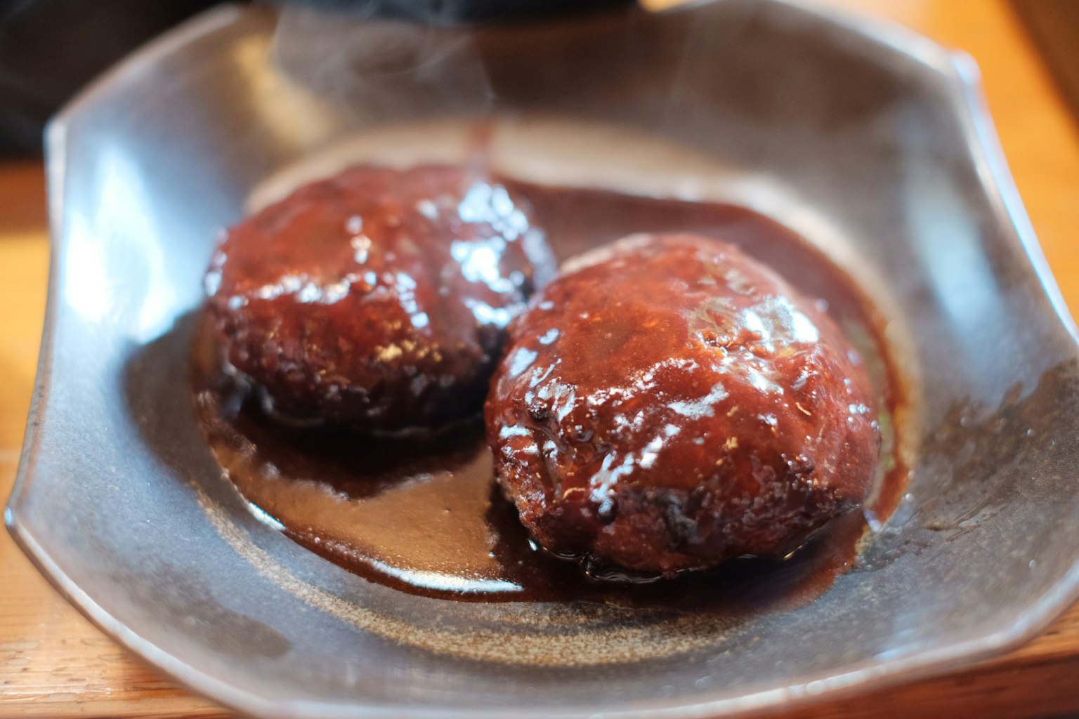 Two hamburgers on a black plate topped with rich sauce