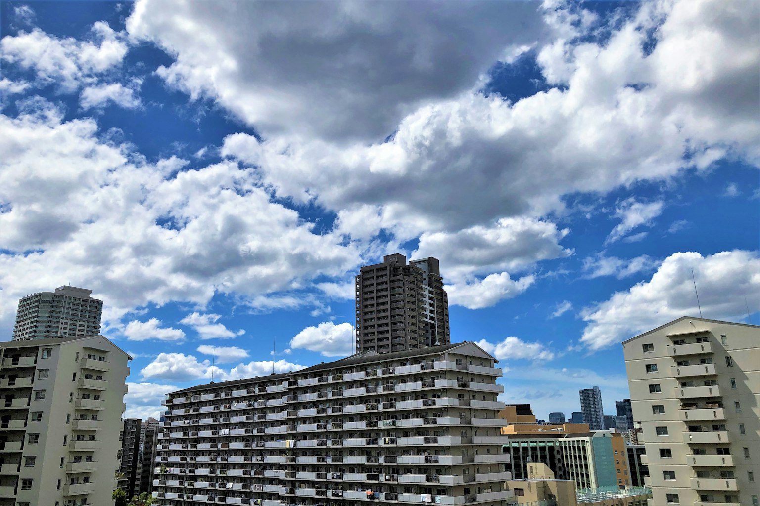 Urban landscape with blue sky and white clouds featuring high-rise buildings and apartments