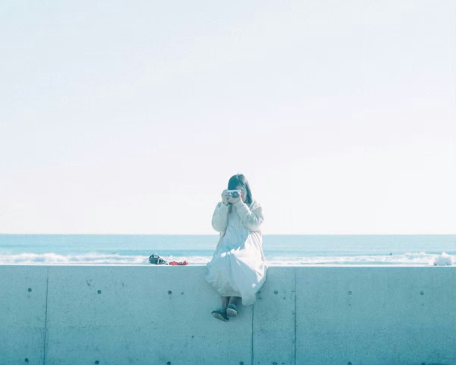 Mujer con vestido blanco sosteniendo una cámara junto al mar