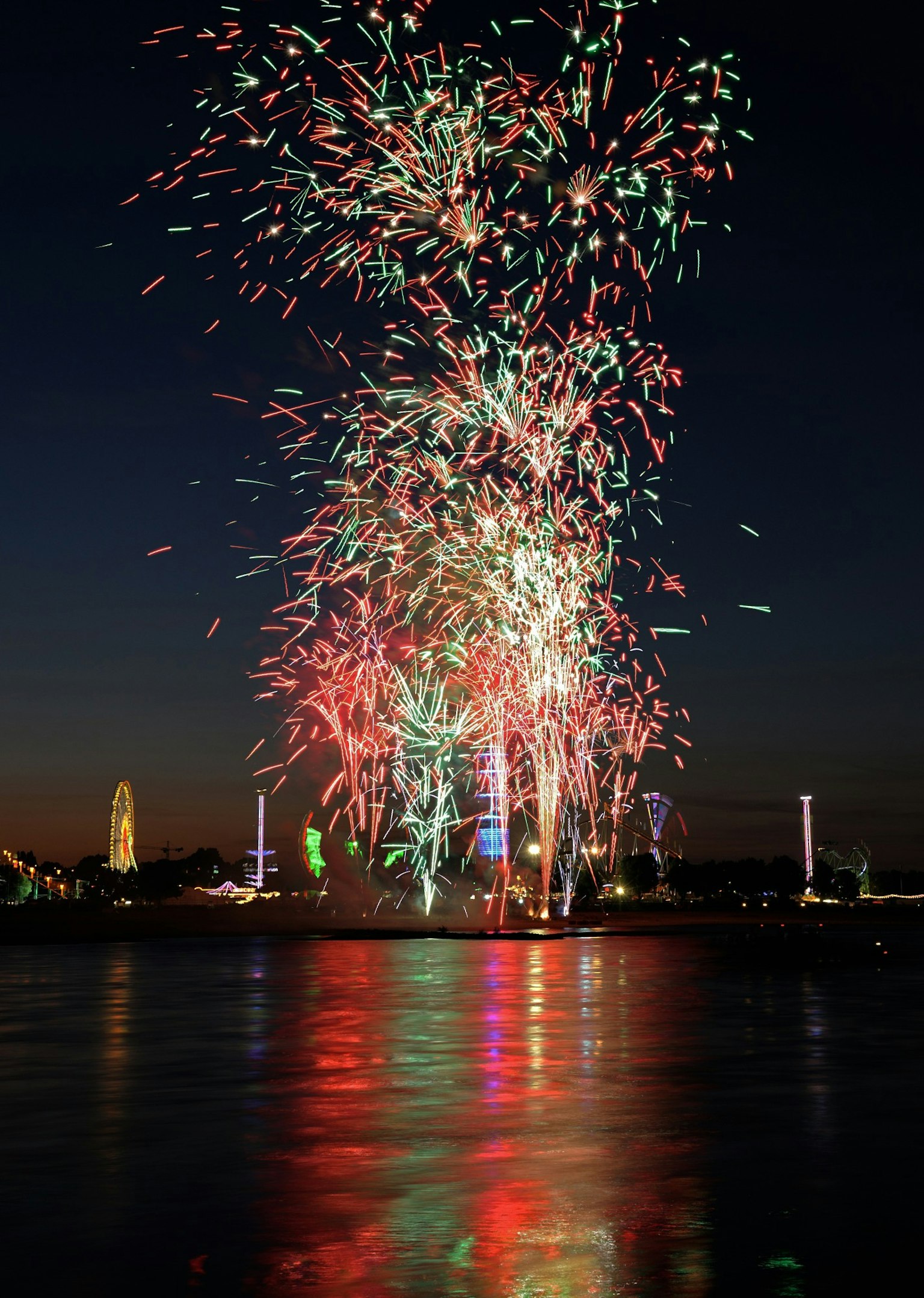 Bunte Feuerwerke, die am Nachthimmel explodieren, mit Reflexionen auf dem Wasser