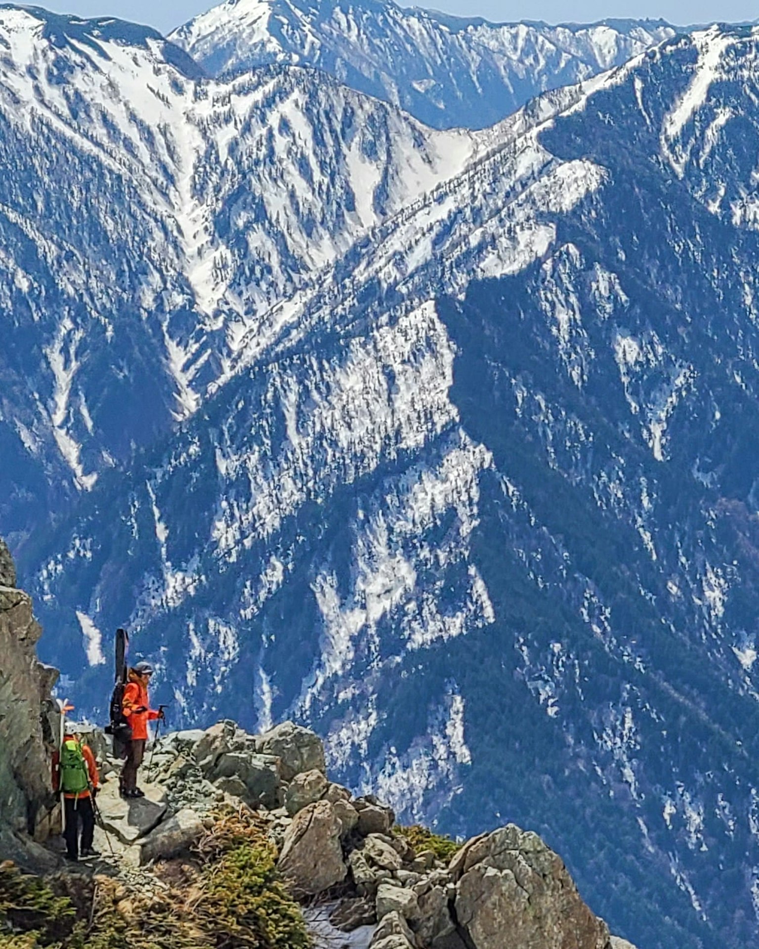 Hikers standing on rocky terrain with snow-covered mountains in the background