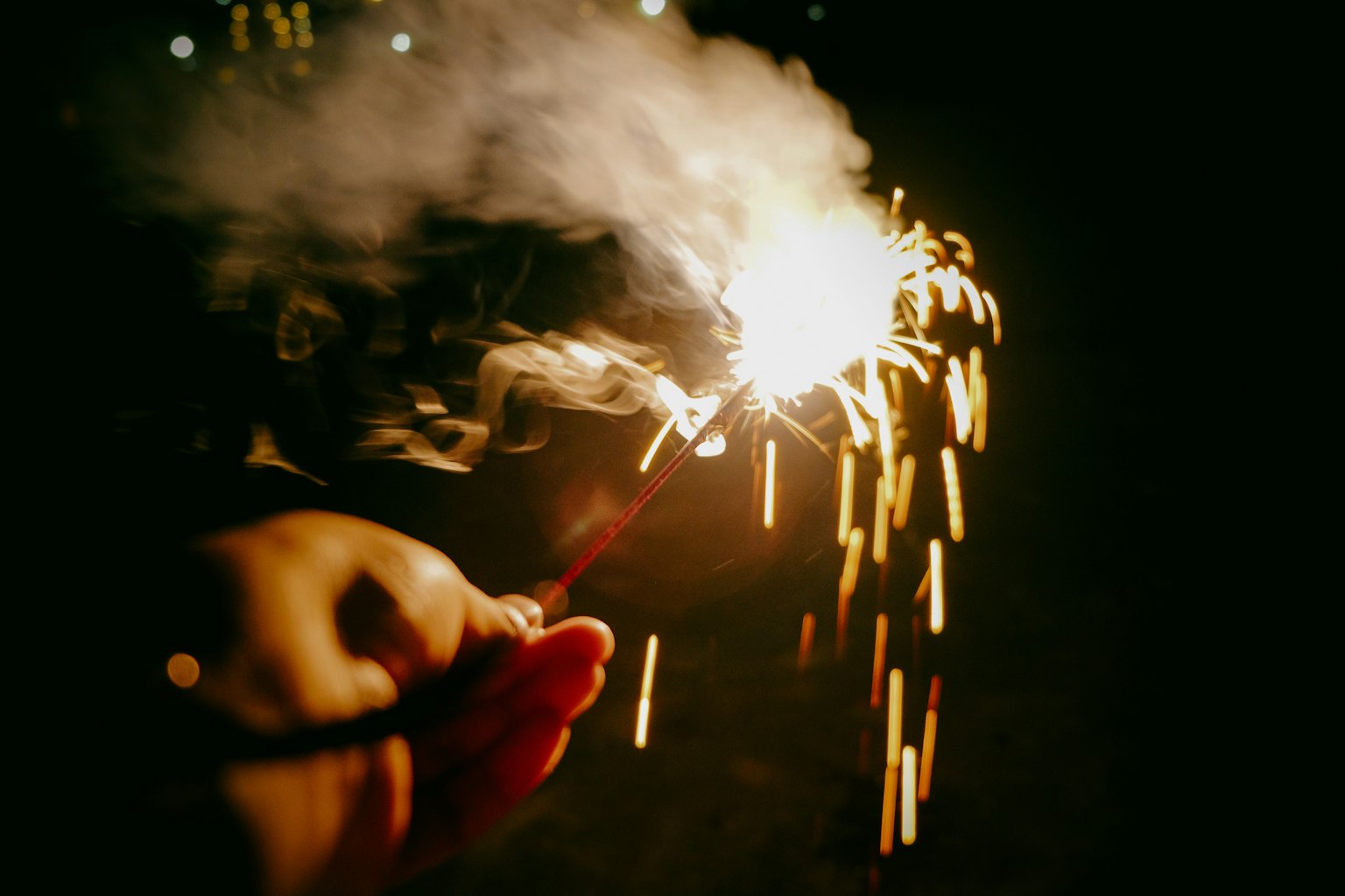 Mano sosteniendo un chispero con chispas y humo por la noche