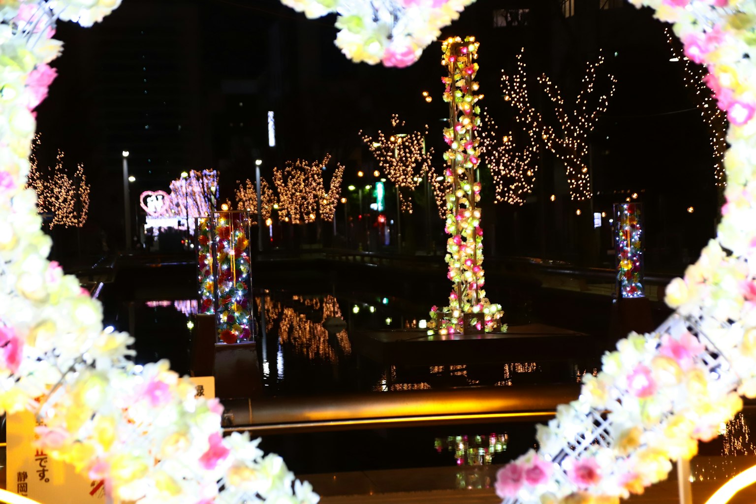 Marco en forma de corazón que muestra árboles iluminados y decoraciones coloridas en un parque nocturno