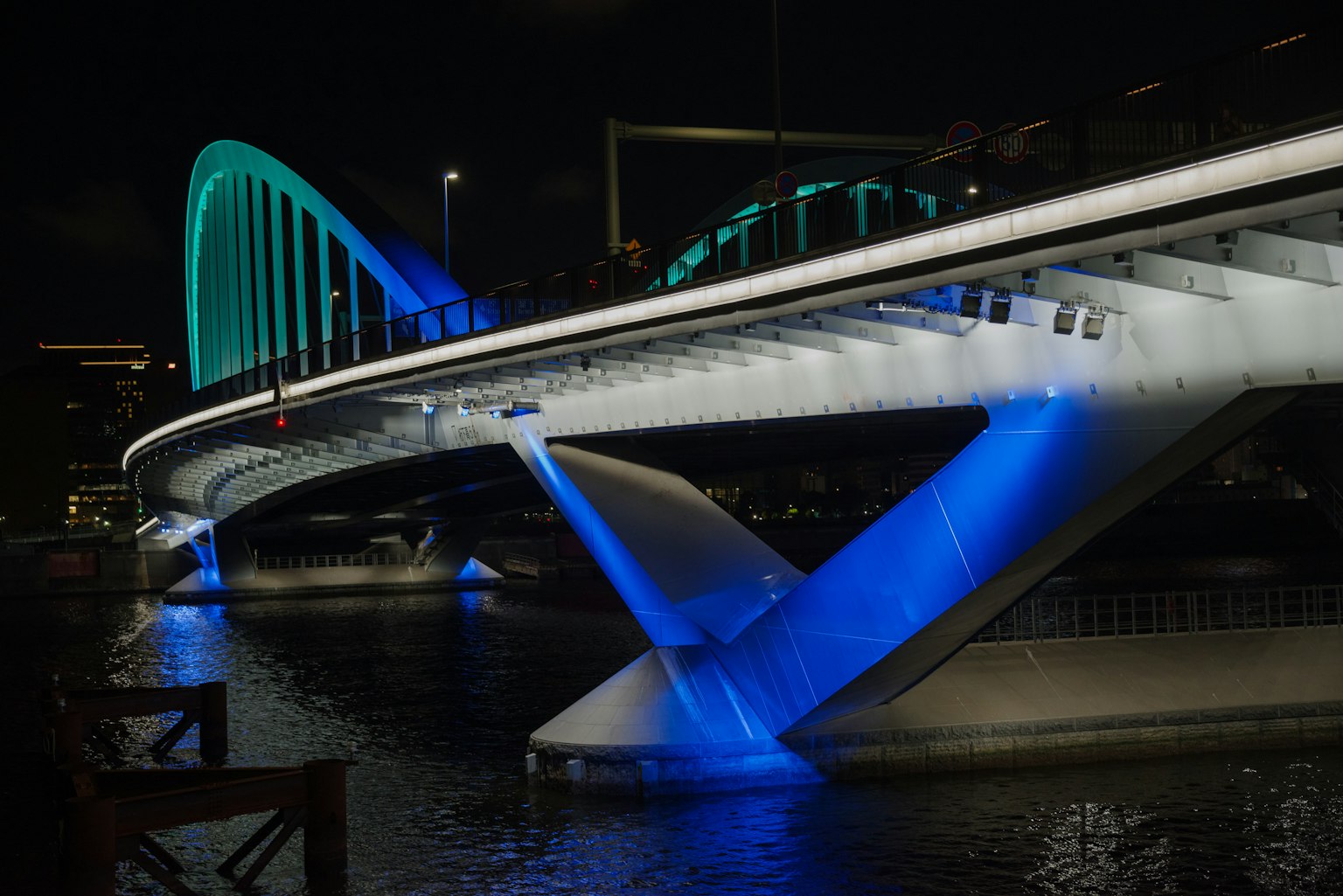 夜间照亮的现代桥梁 蓝色和绿色灯光在水面上反射