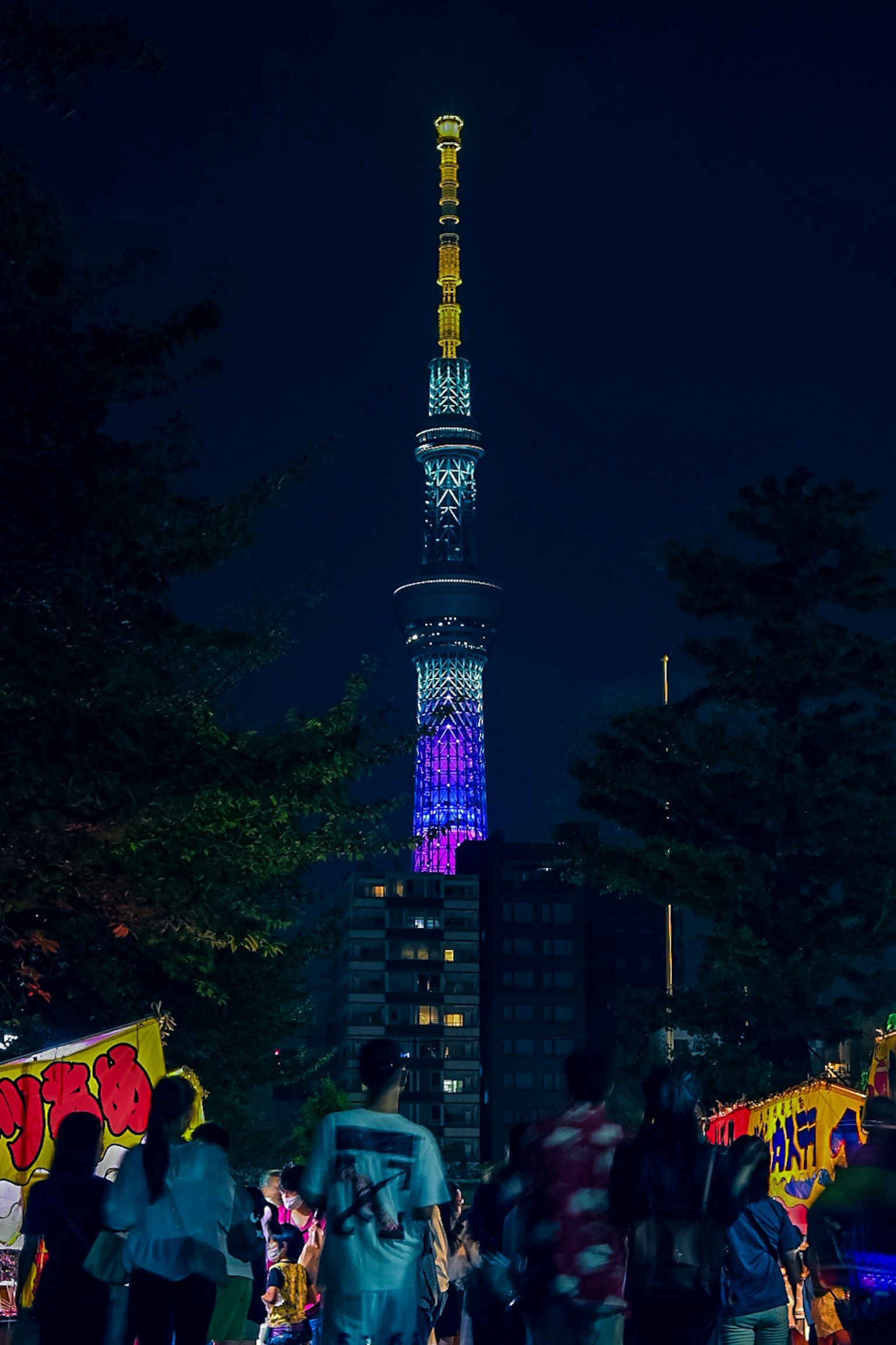 Tokyo Skytree illuminé la nuit avec des lumières colorées et des gens marchant devant