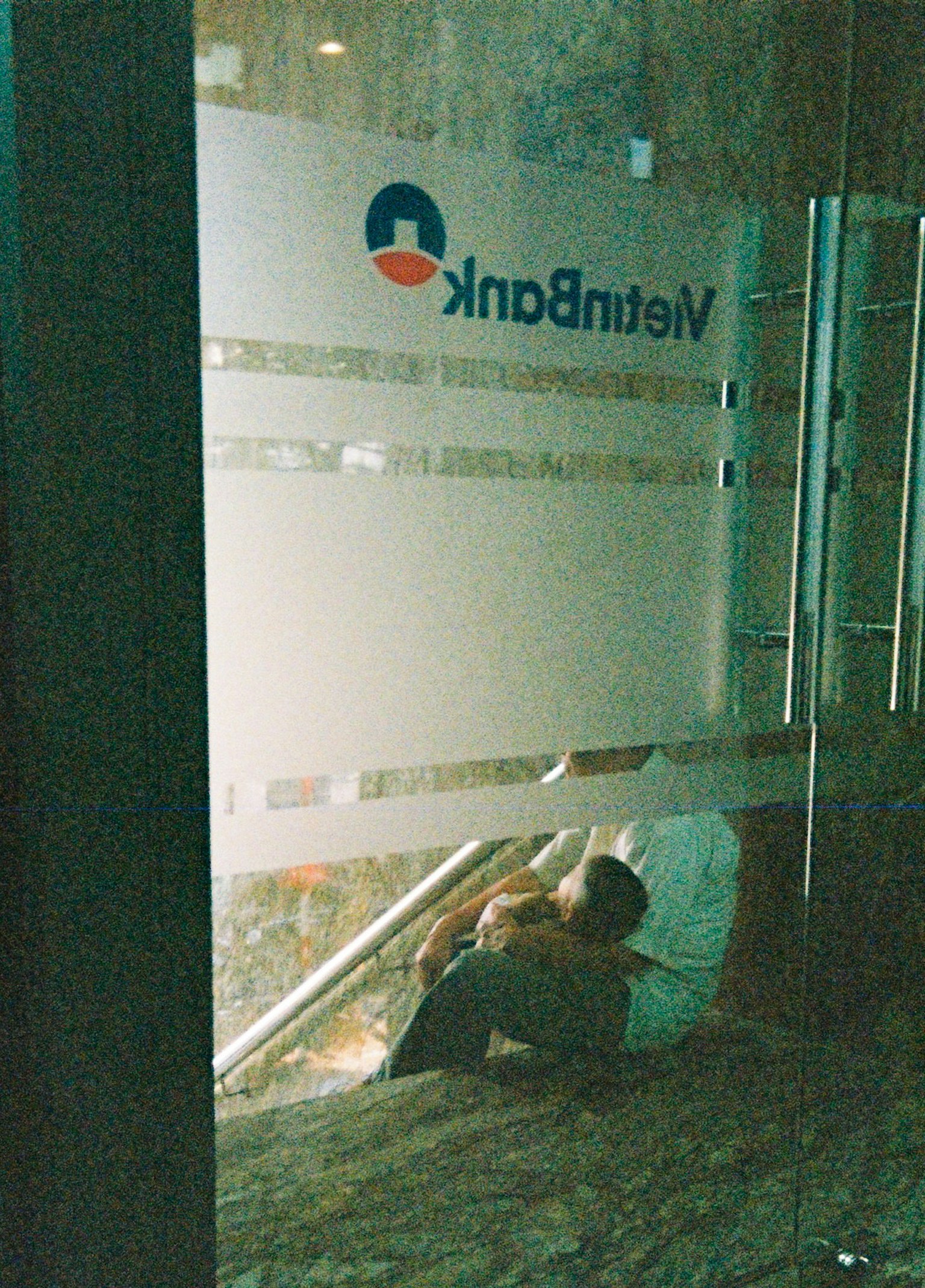 ベトナム銀行のロゴが見えるガラスのドアの前に座っている人