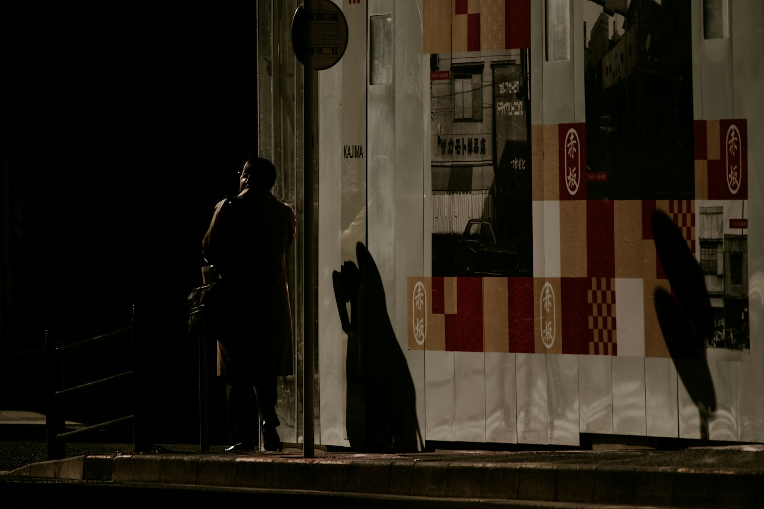 Une silhouette debout dans une rue sombre avec un mur ombragé