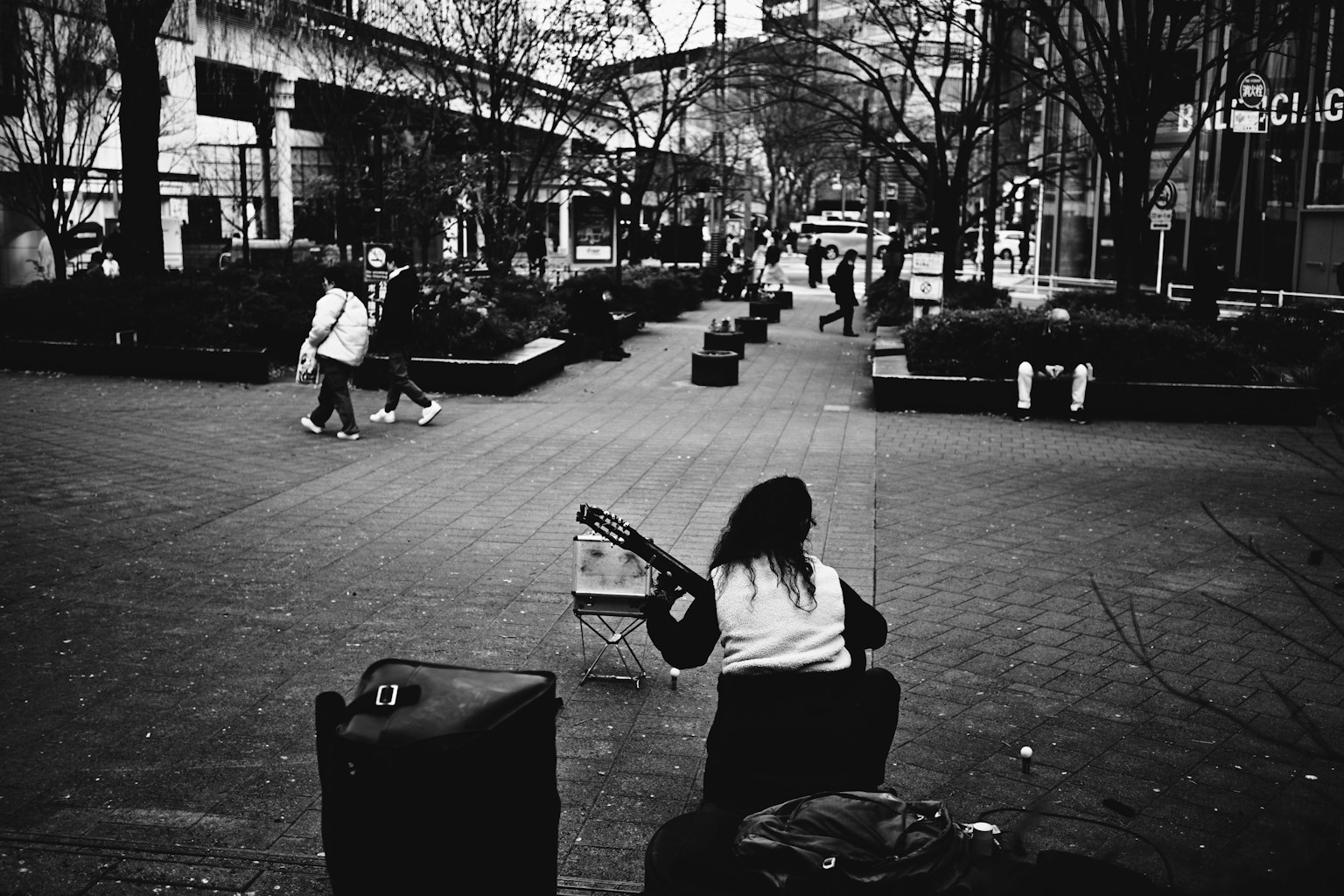 Wanita bermain gitar di lingkungan perkotaan hitam putih dengan pejalan kaki