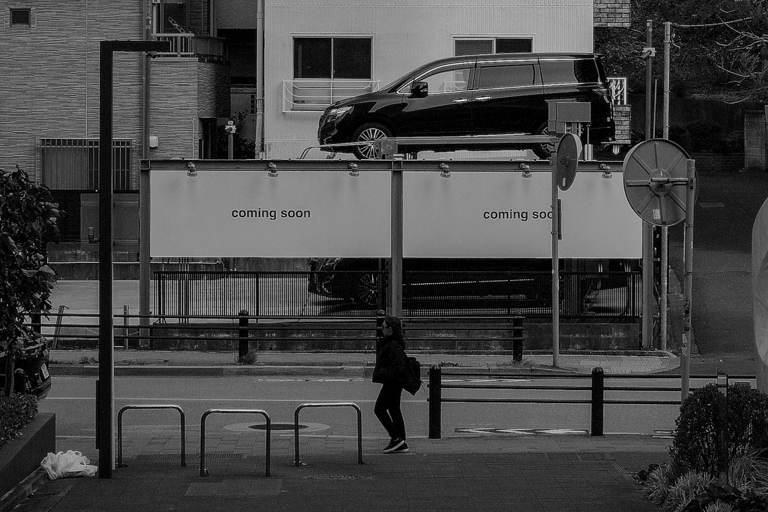 A person walking on a street corner with a car parked above on a structure
