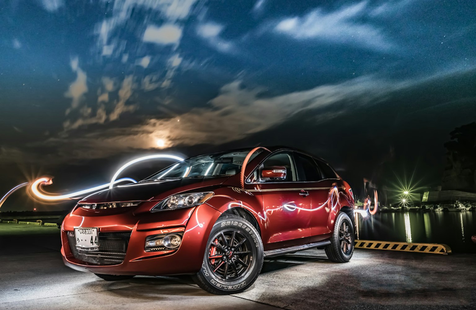 SUV rouge garé la nuit sous la lumière de la lune avec des traînées lumineuses