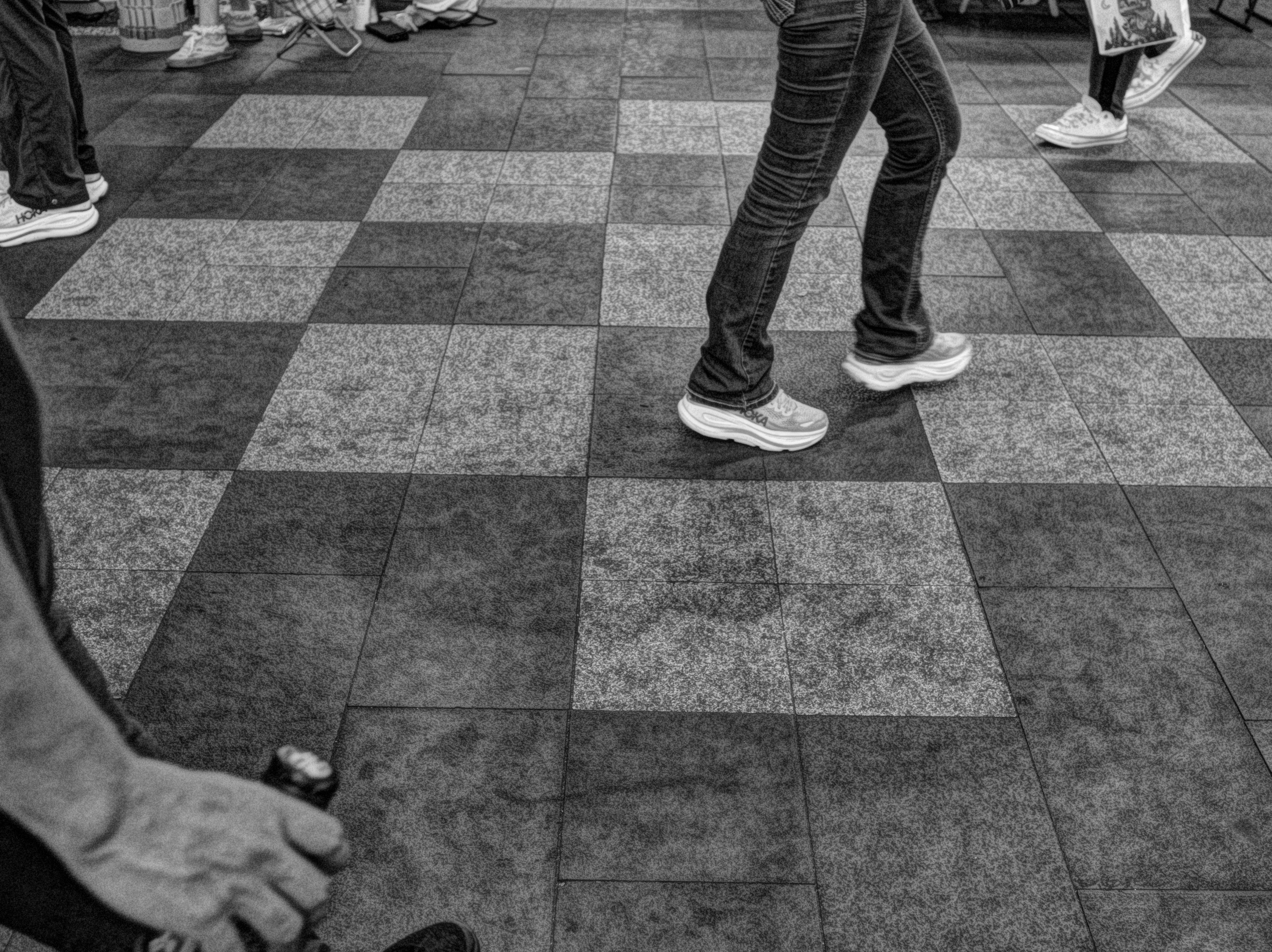 モノクロの街角で歩く人と手が写る路面のスナップ
