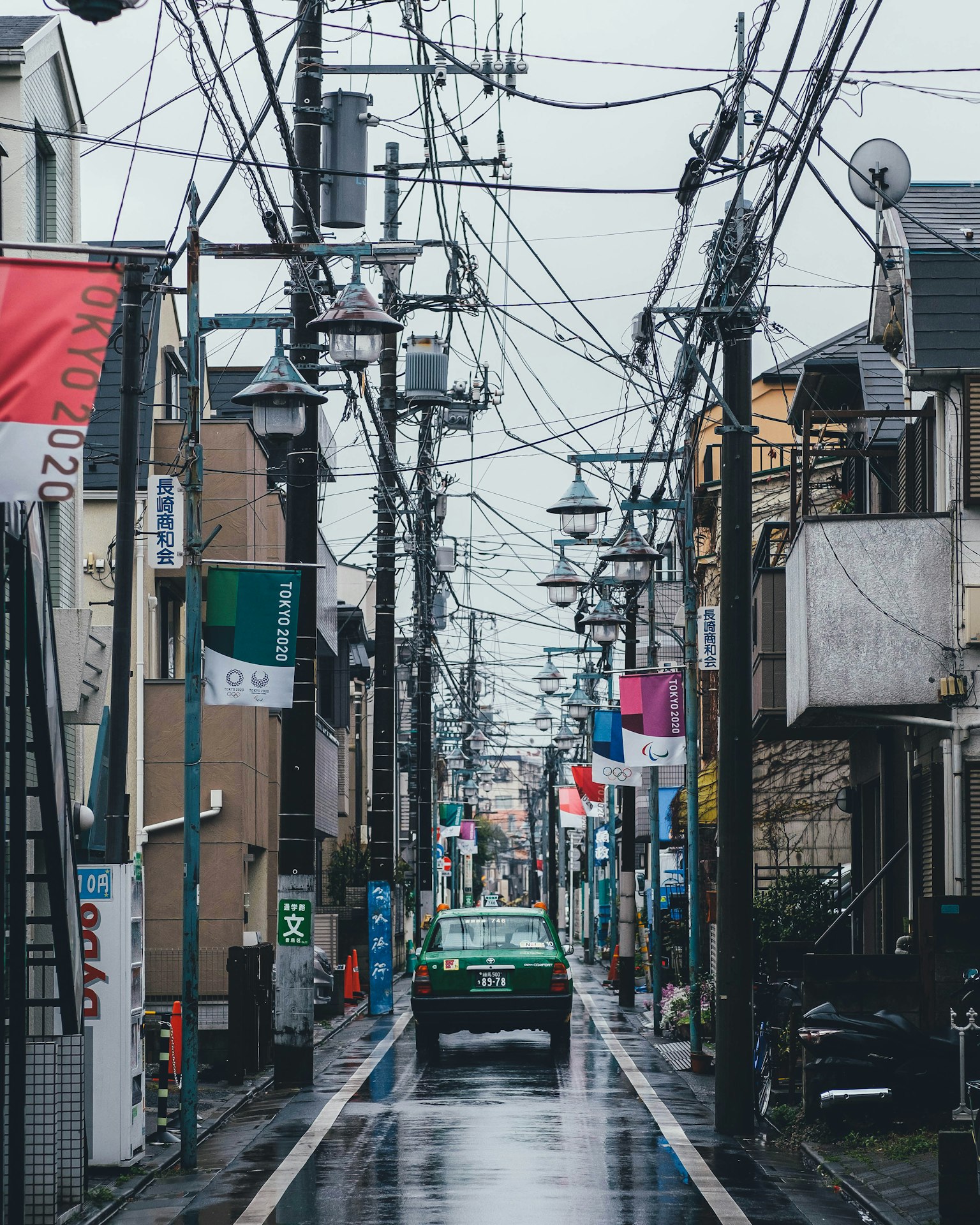 Street view with a green car on a rainy day surrounded by power lines and colorful banners